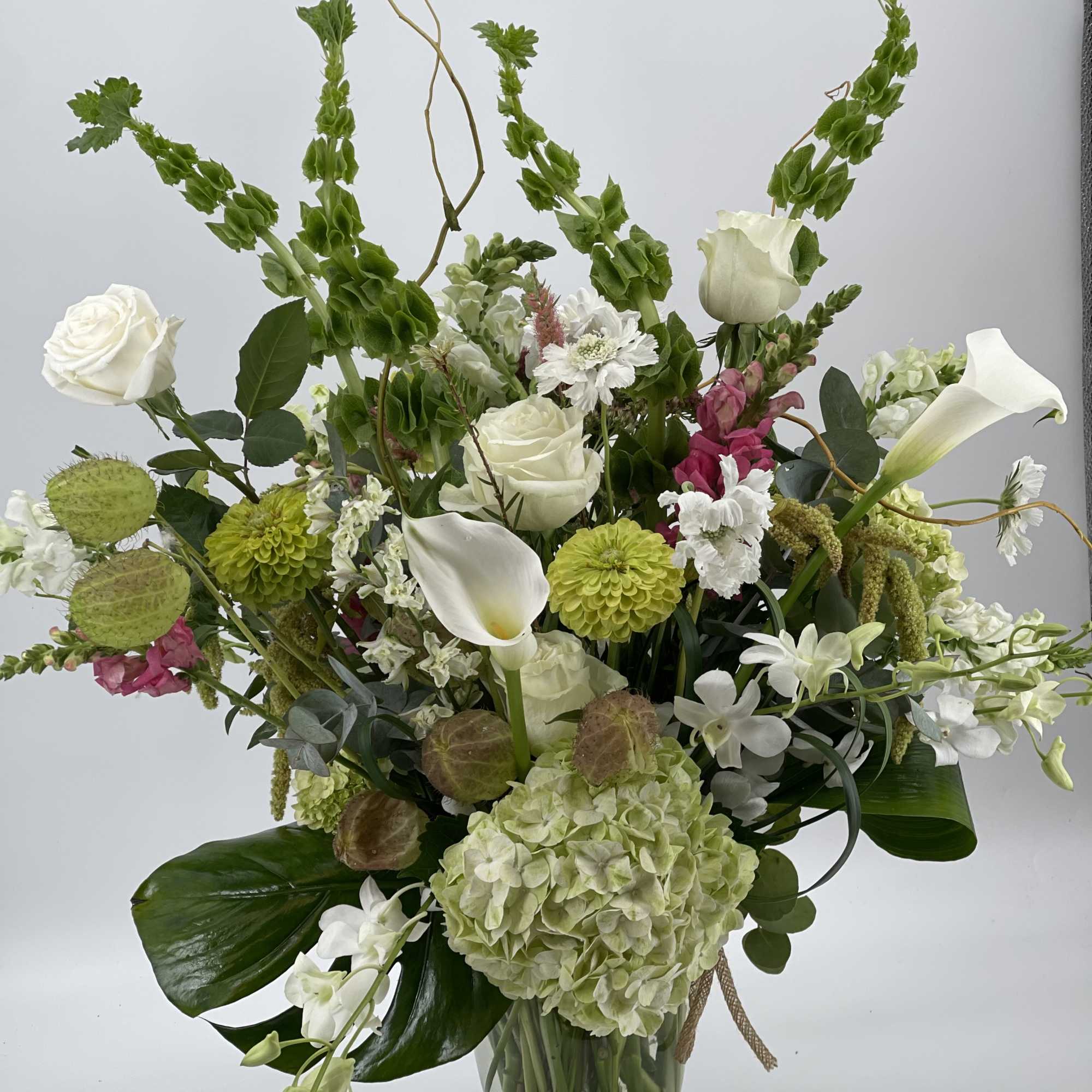 Tall mixed floral arrangement in a glass vase with white roses, calla lilies, and green blooms