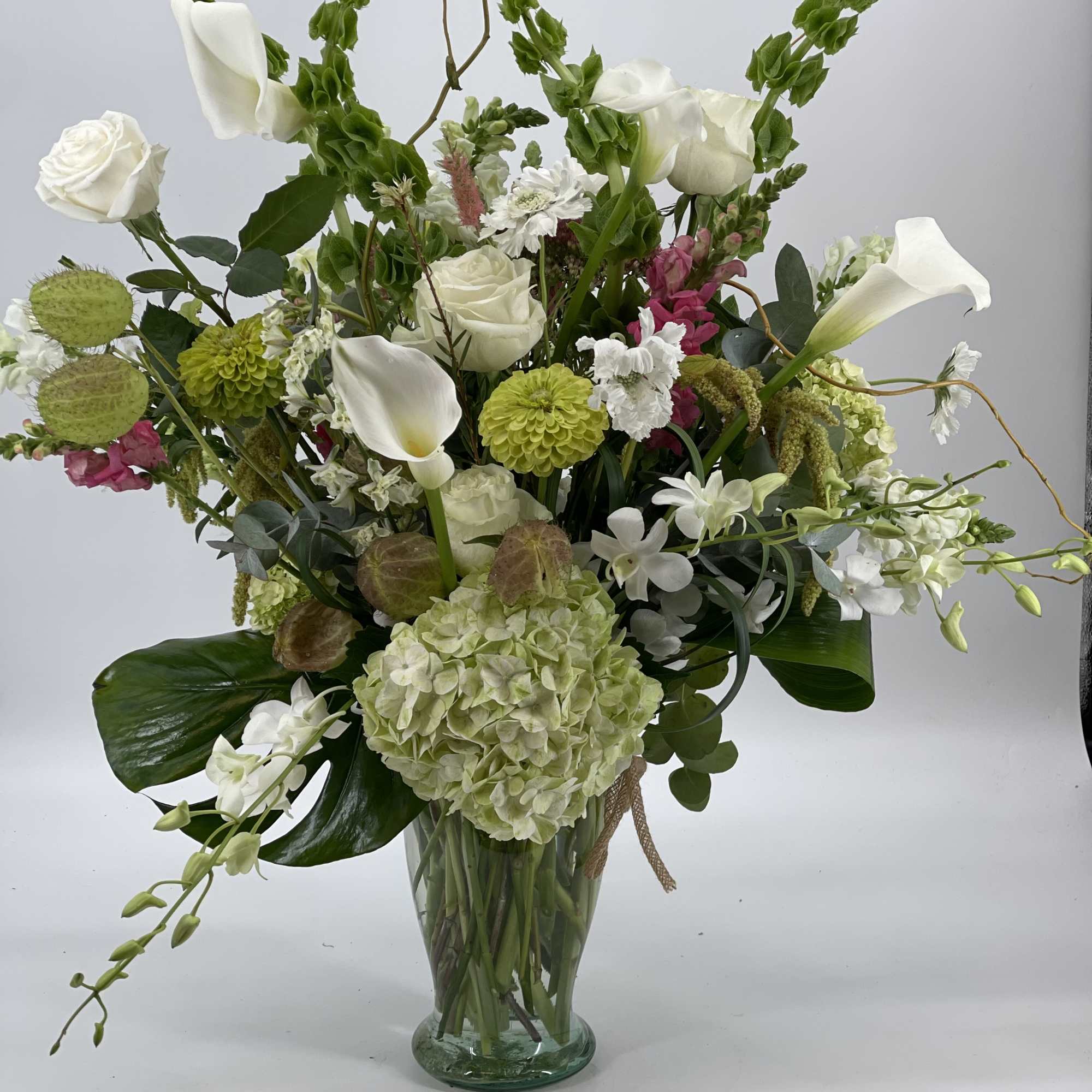 Tall mixed floral arrangement in a glass vase with white callas and roses