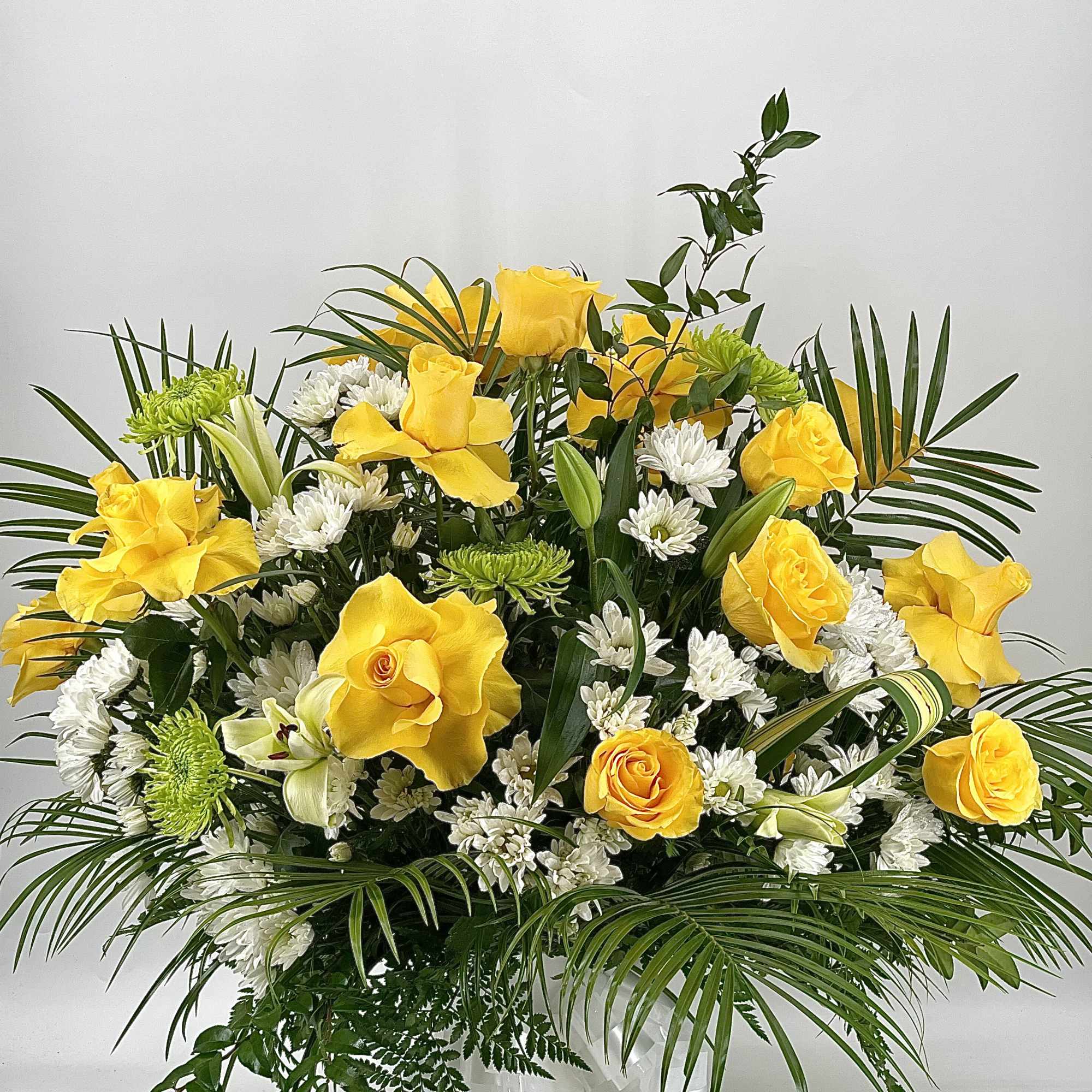 Yellow roses and white flowers in a white vase with palm fronds