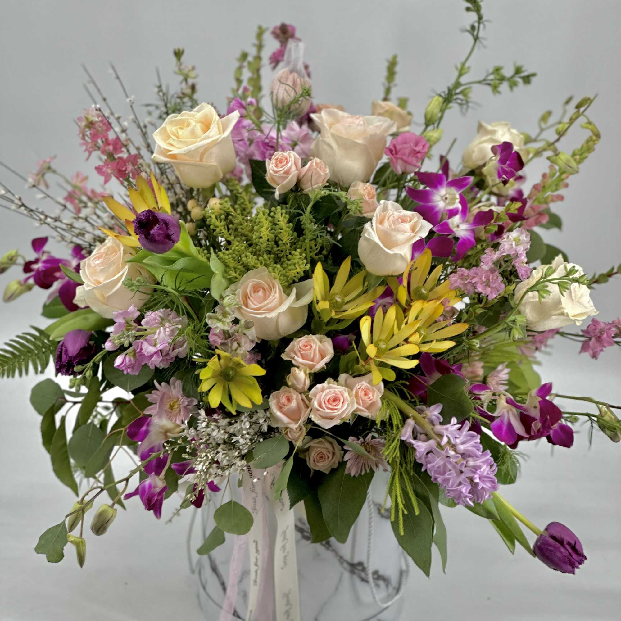 Mixed bouquet of roses, orchids, and yellow flowers in a marble-patterned vase