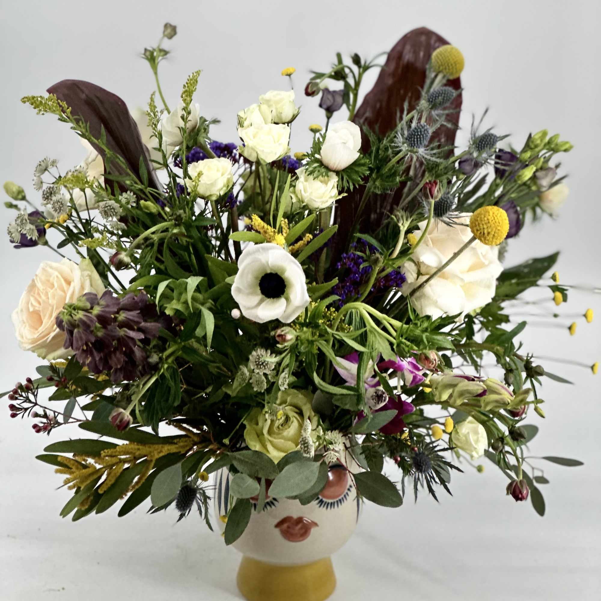 Mixed bouquet of white, cream, purple, and yellow flowers in a ceramic vase