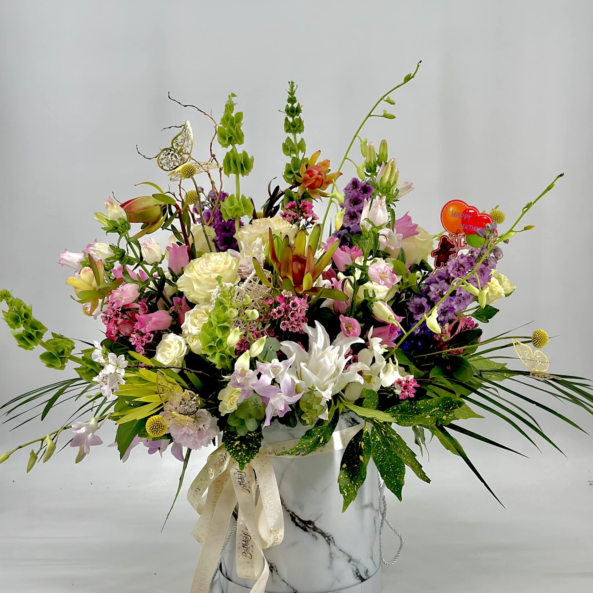 Large mixed flower arrangement in a white marble-patterned hatbox