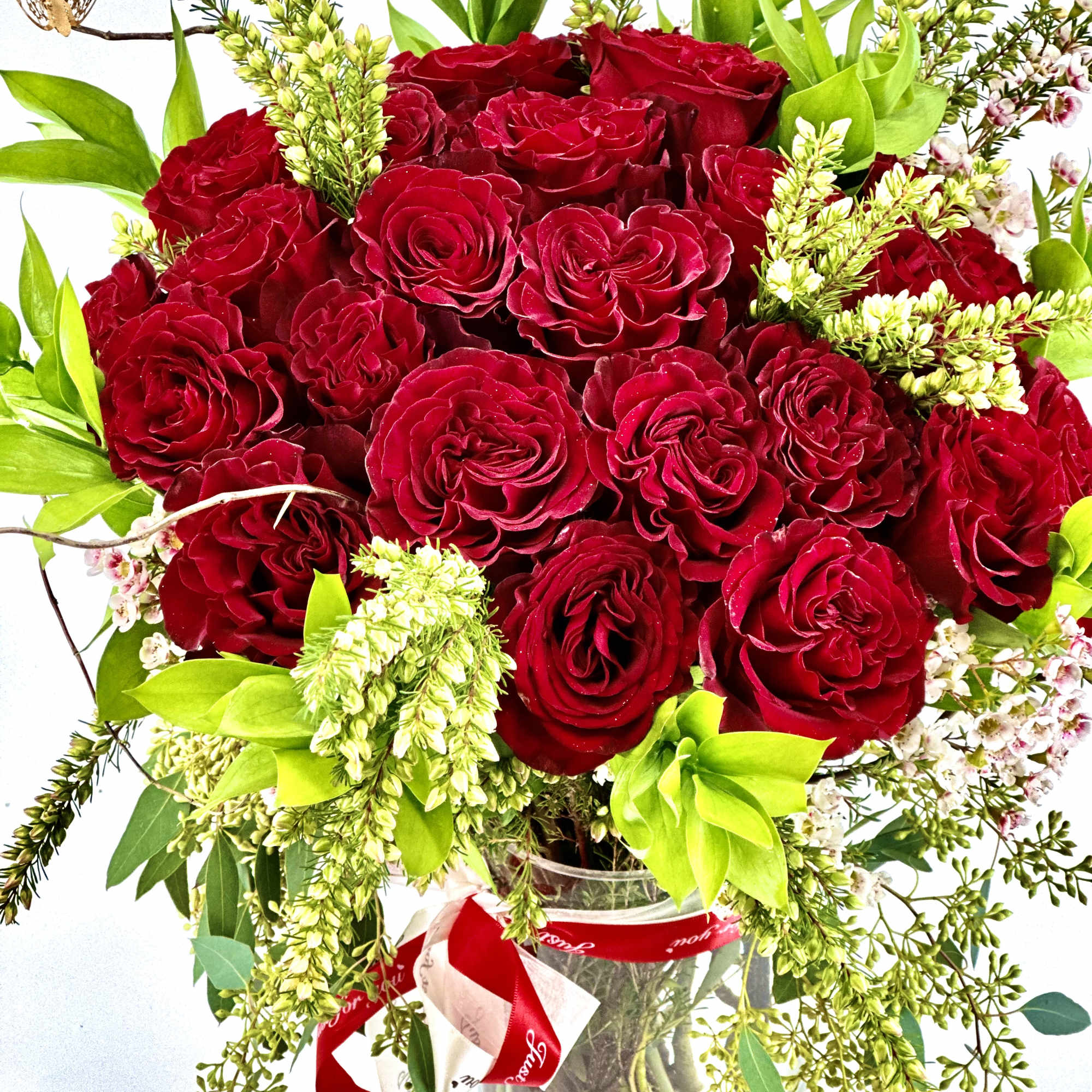 Red rose bouquet in a clear glass vase with bright green accents