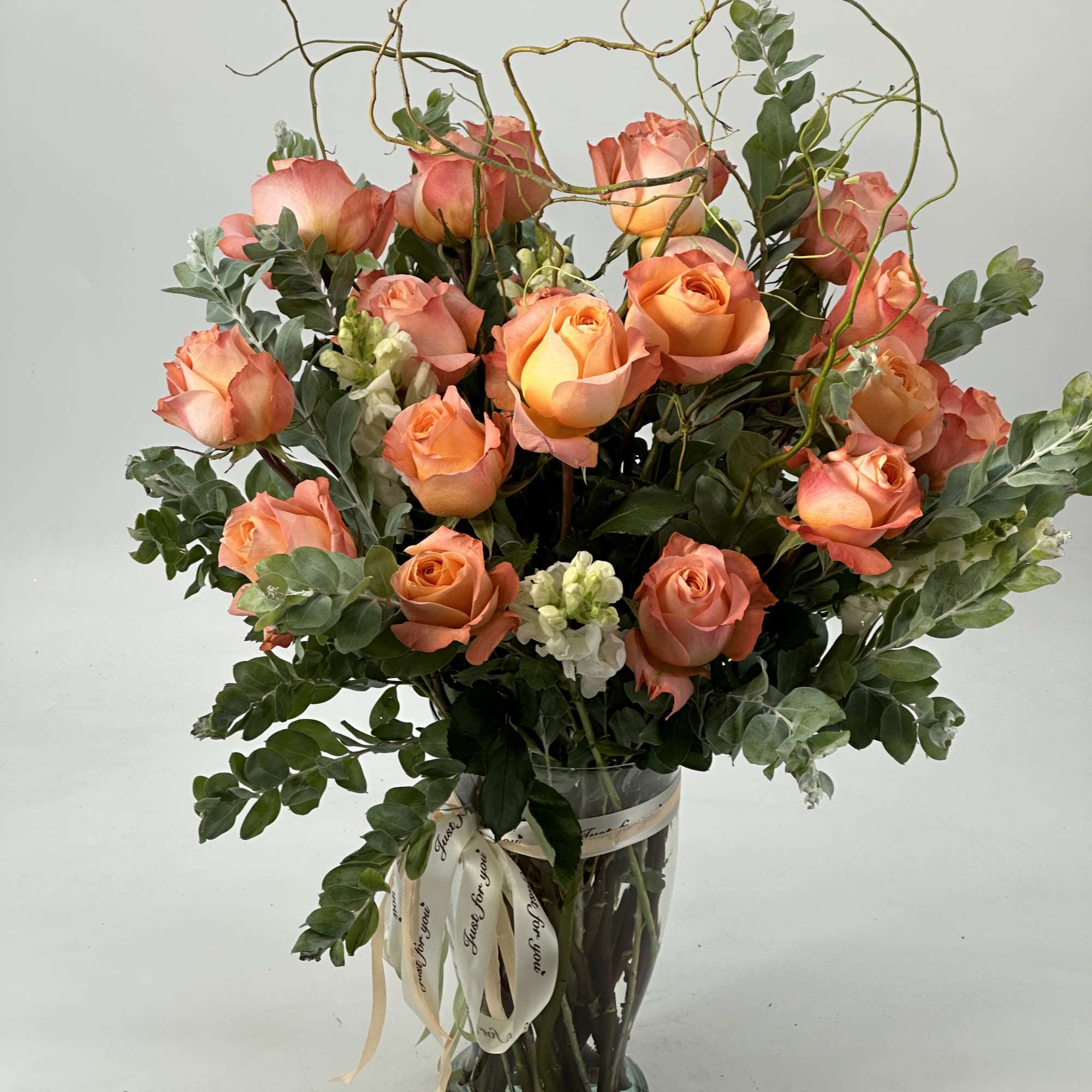 Tall bouquet of peach roses in a glass vase with ribbon