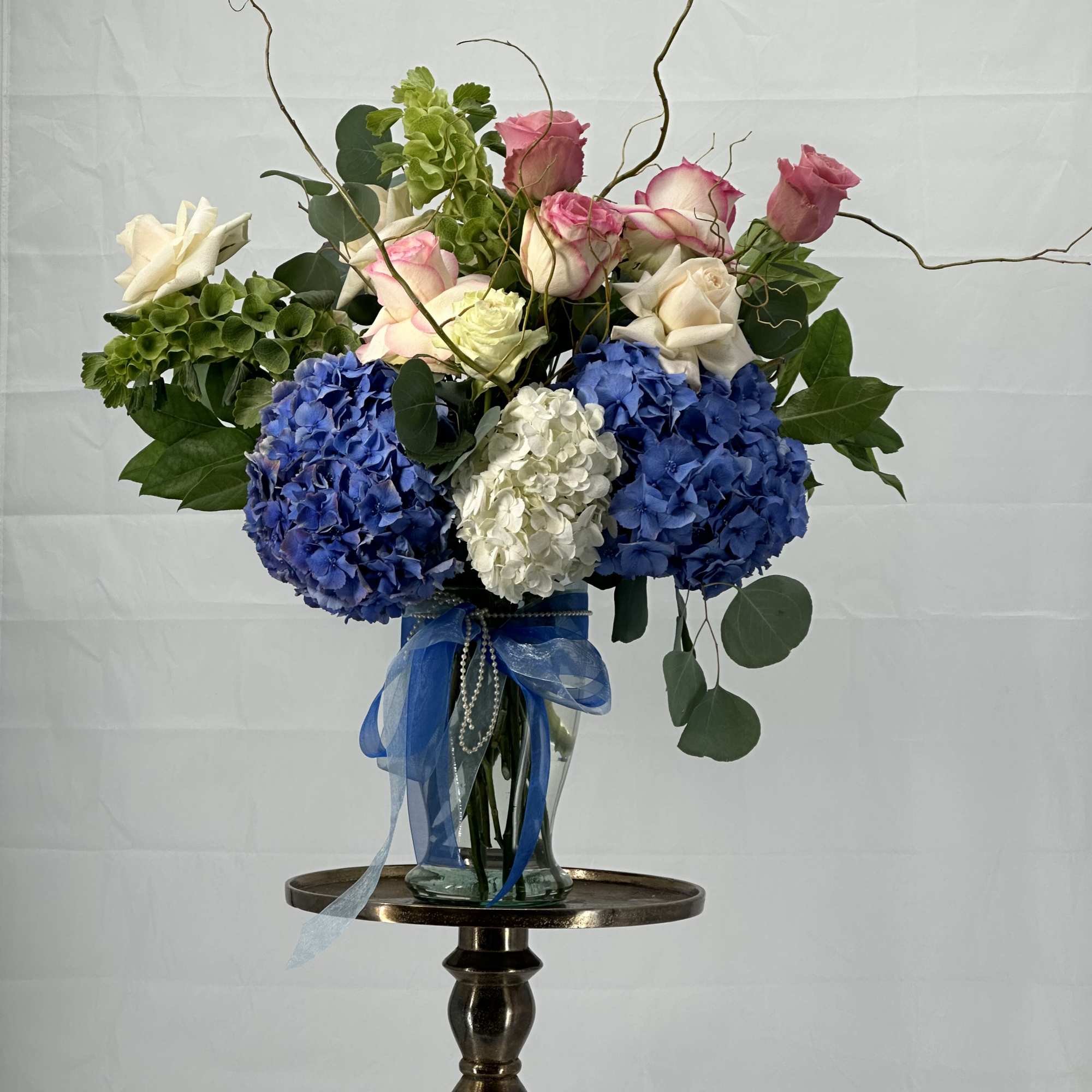 Bouquet of roses and hydrangeas in a glass vase with blue ribbon