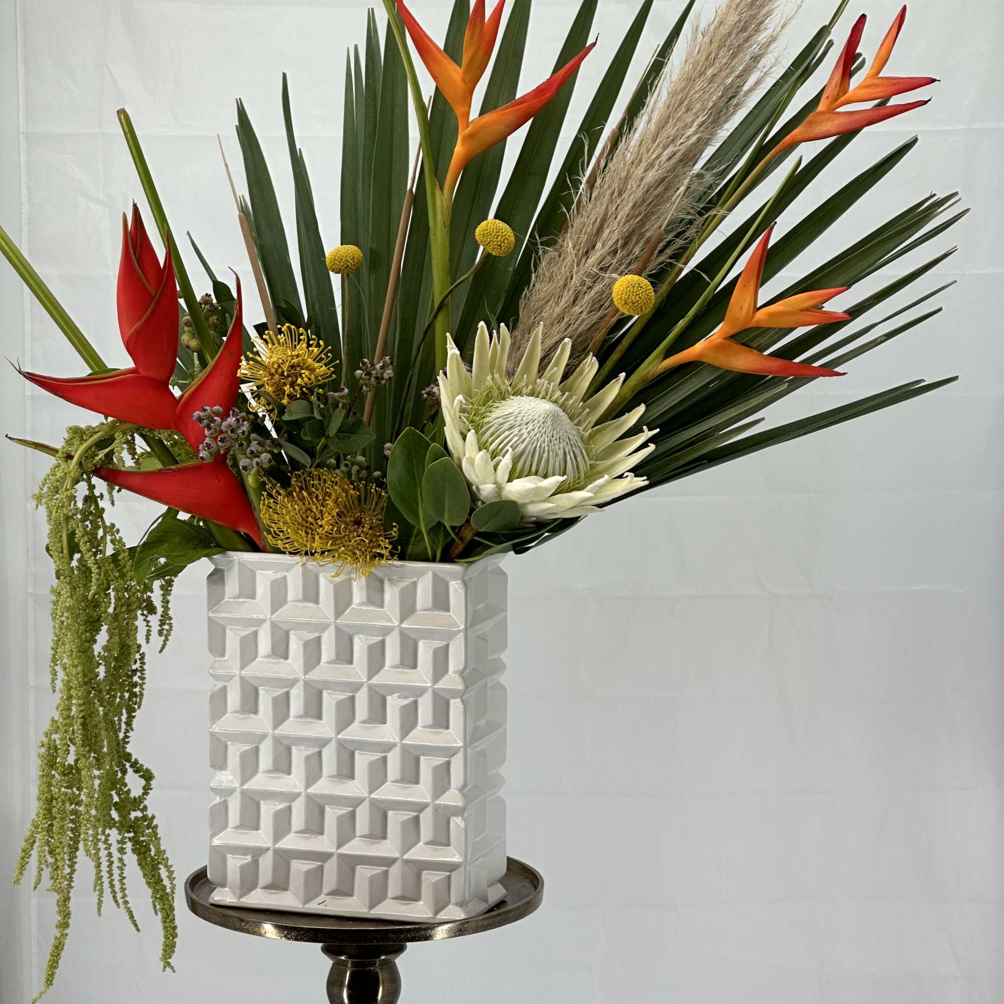 Tropical flower arrangement in a white geometric vase on a pedestal