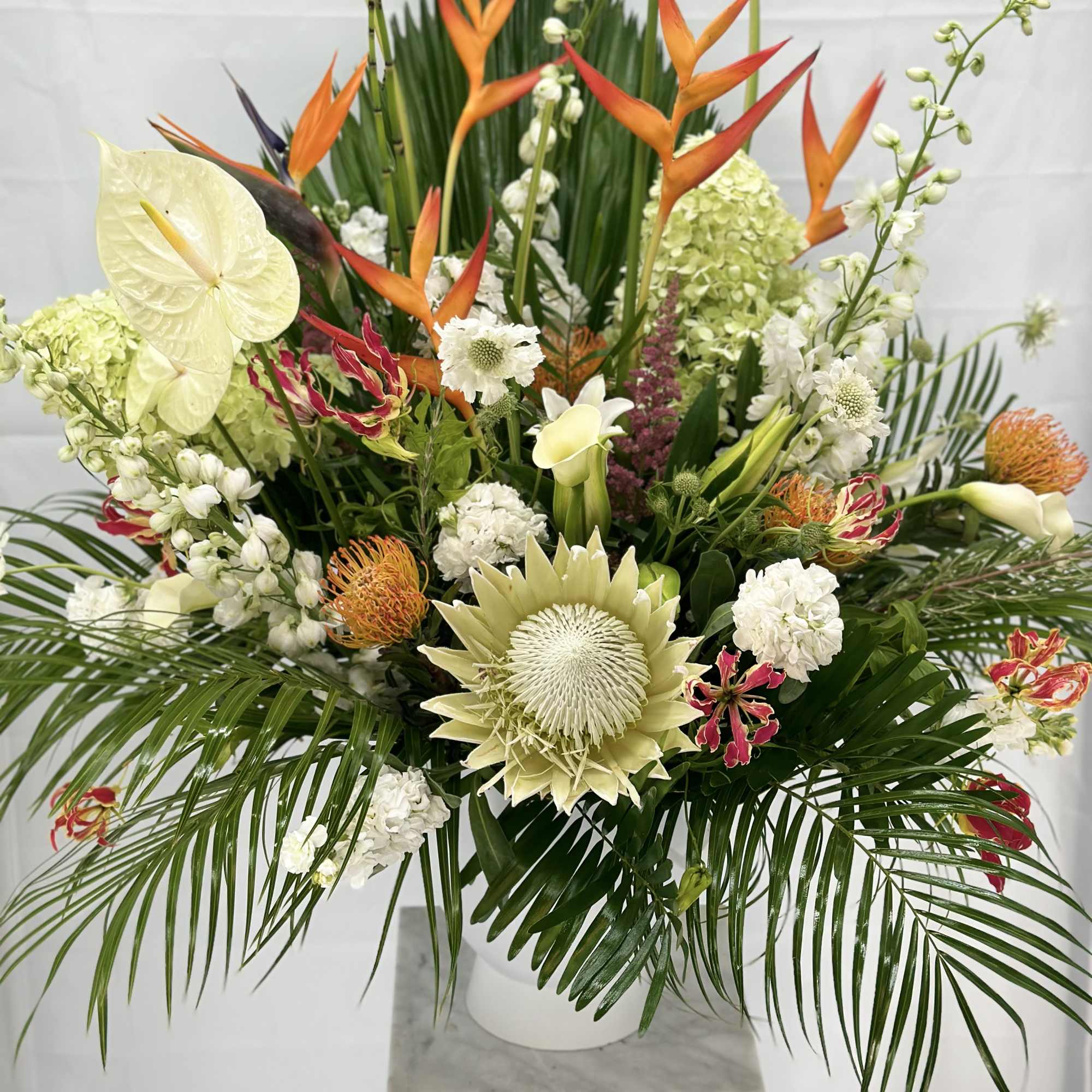 Large tropical floral arrangement with orange bird-of-paradise and white blooms in a white vase