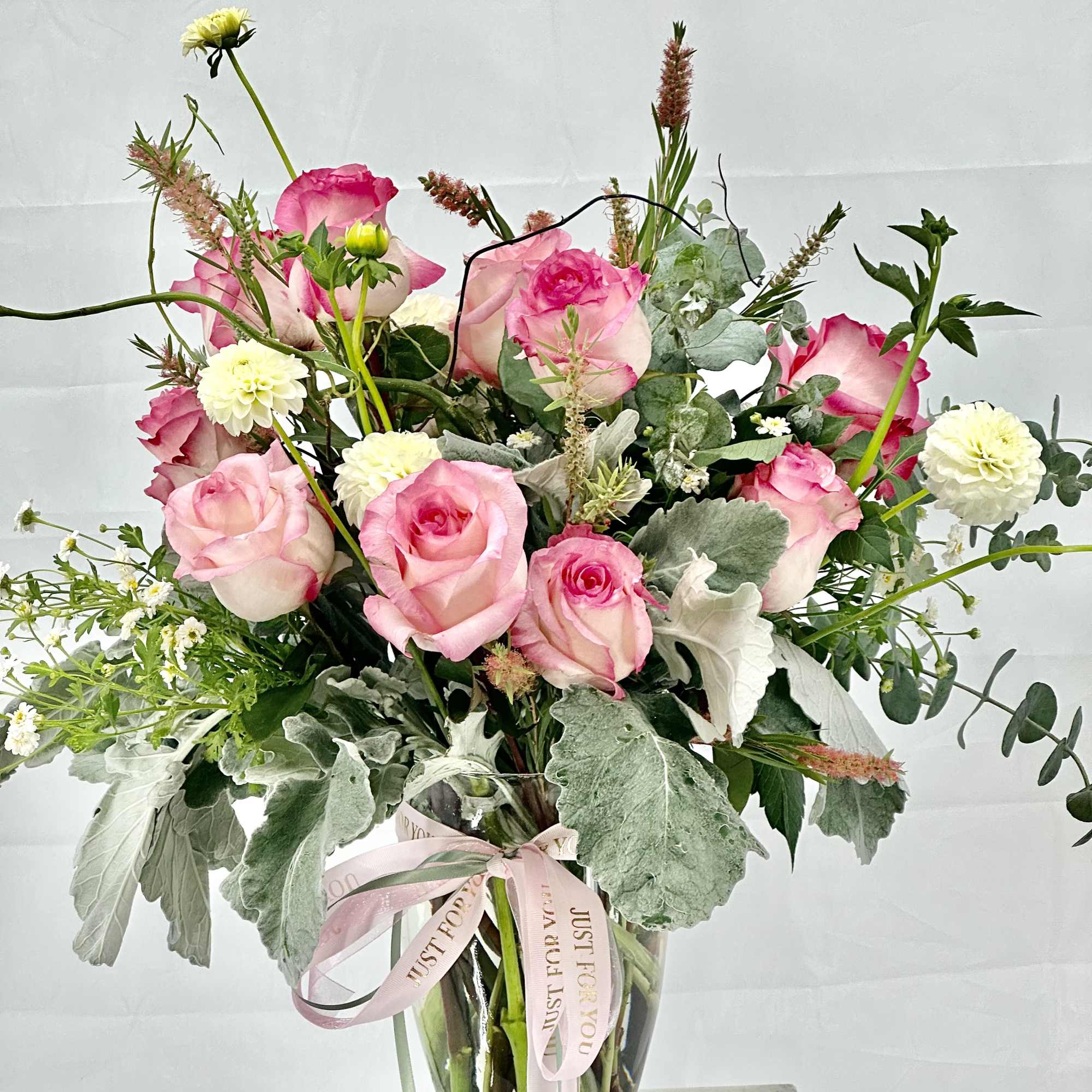 Pink roses and white blooms in a clear glass vase with a pink ribbon