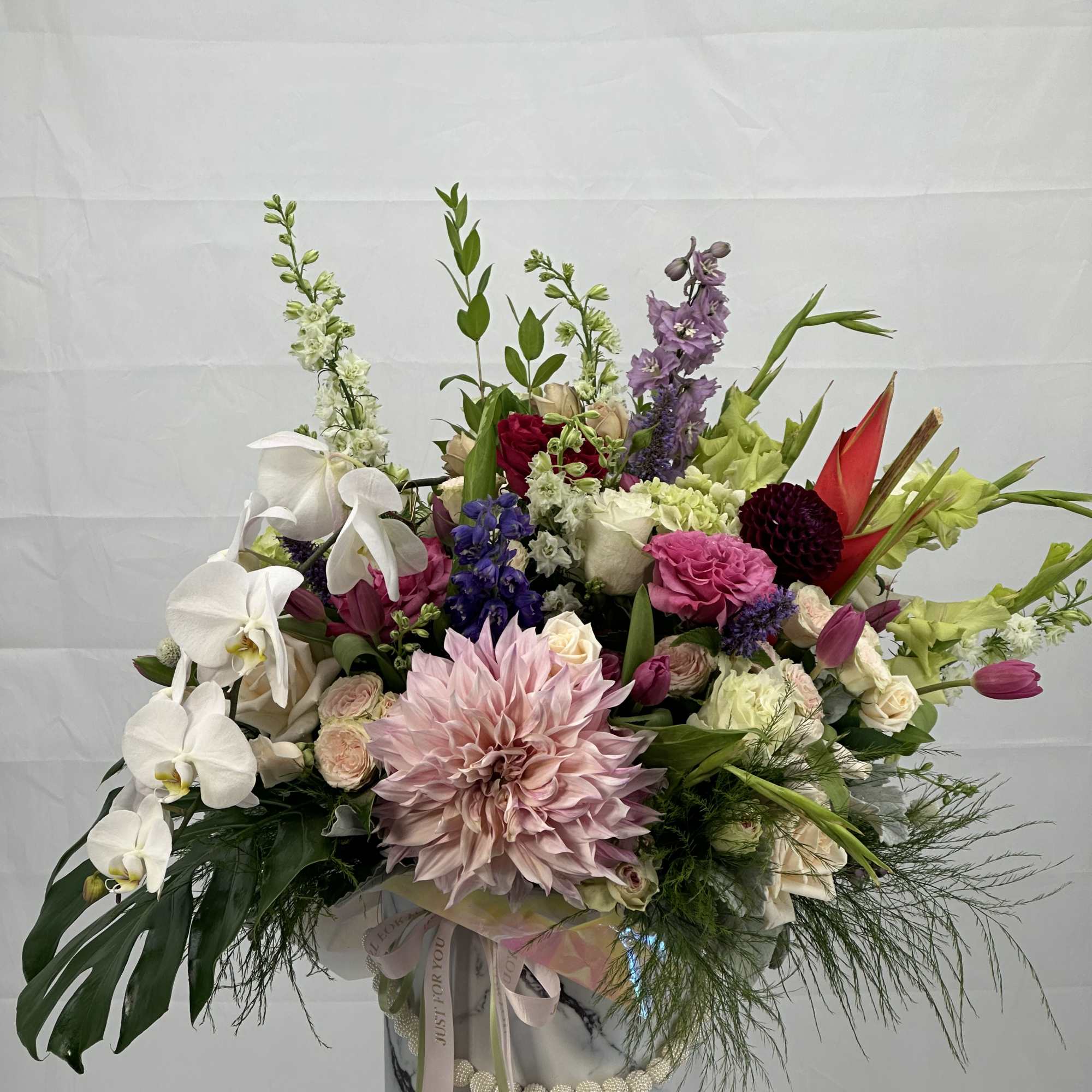 Large mixed bouquet with orchids, dahlias, roses, and lilies in a marble-patterned box