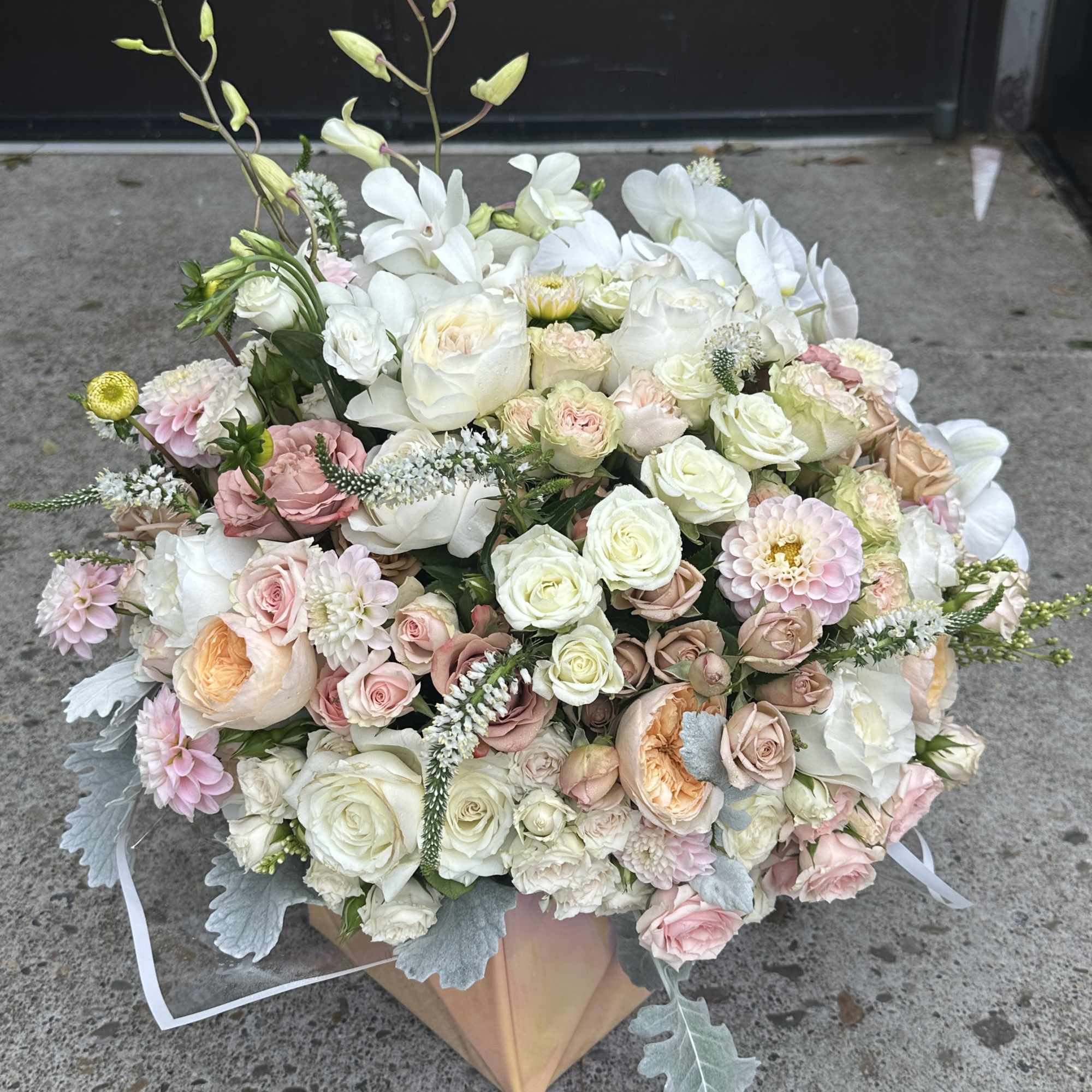 Large pastel bouquet of roses, orchids, and white blooms in a wrapped base