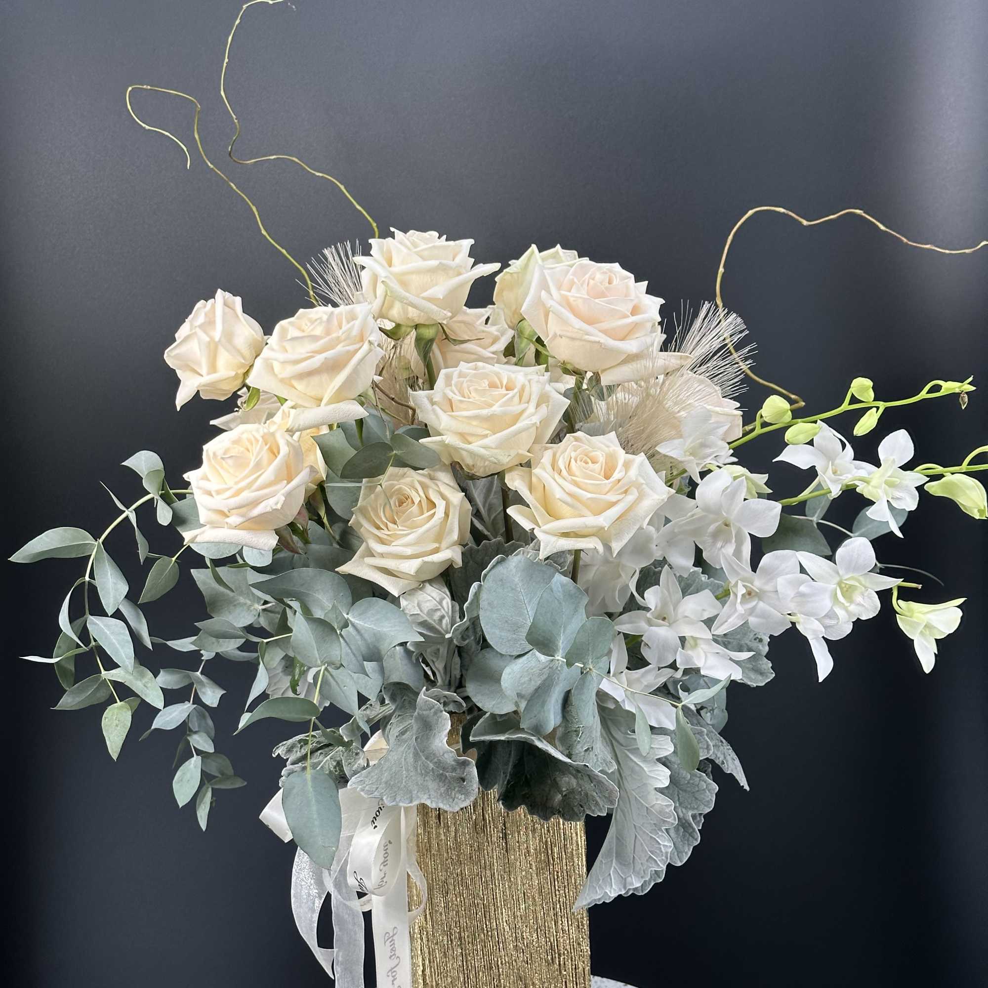 Cream roses and white orchids in a gold vase with silvery foliage, photo 6 of 11
