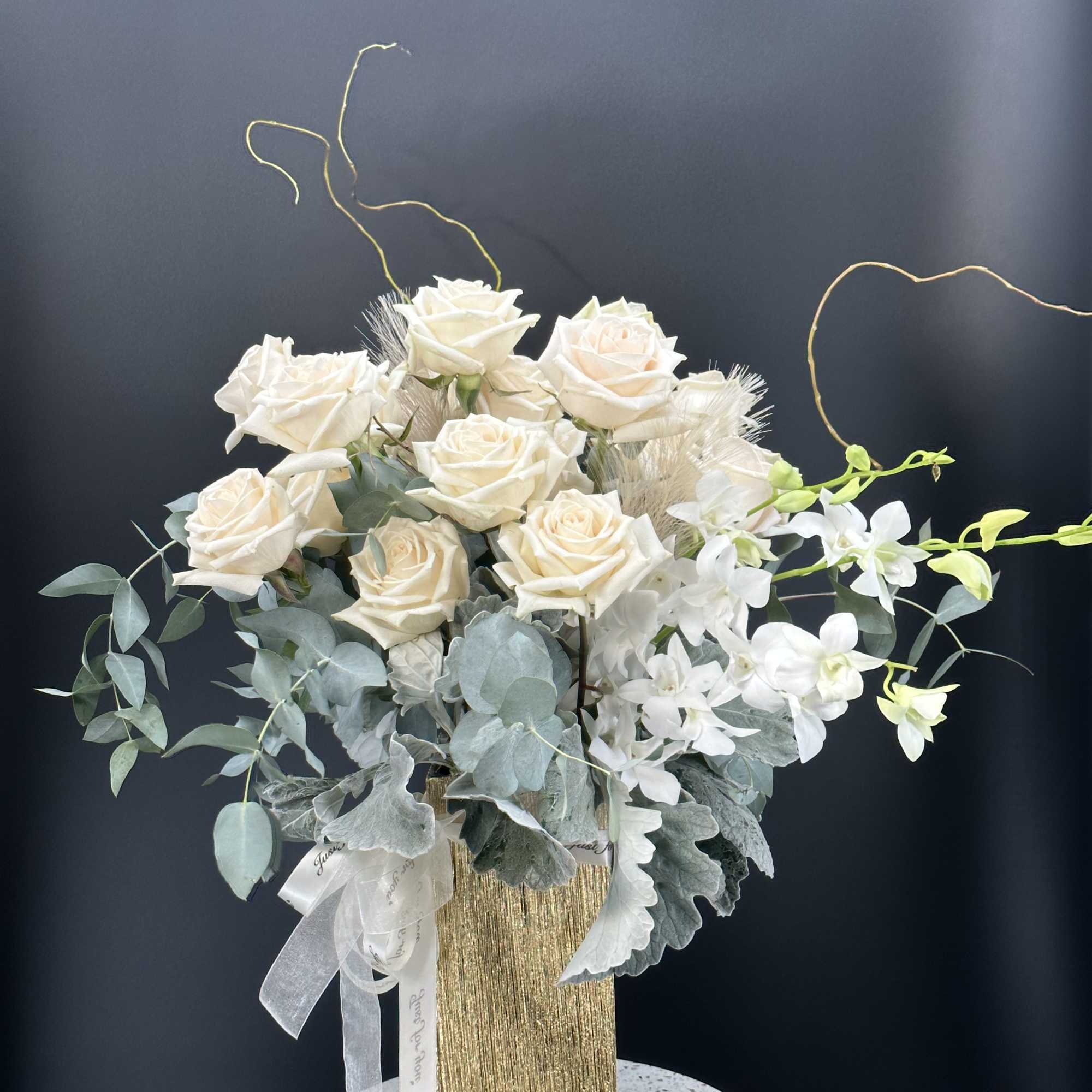 White roses and orchids in a gold vase with pale foliage