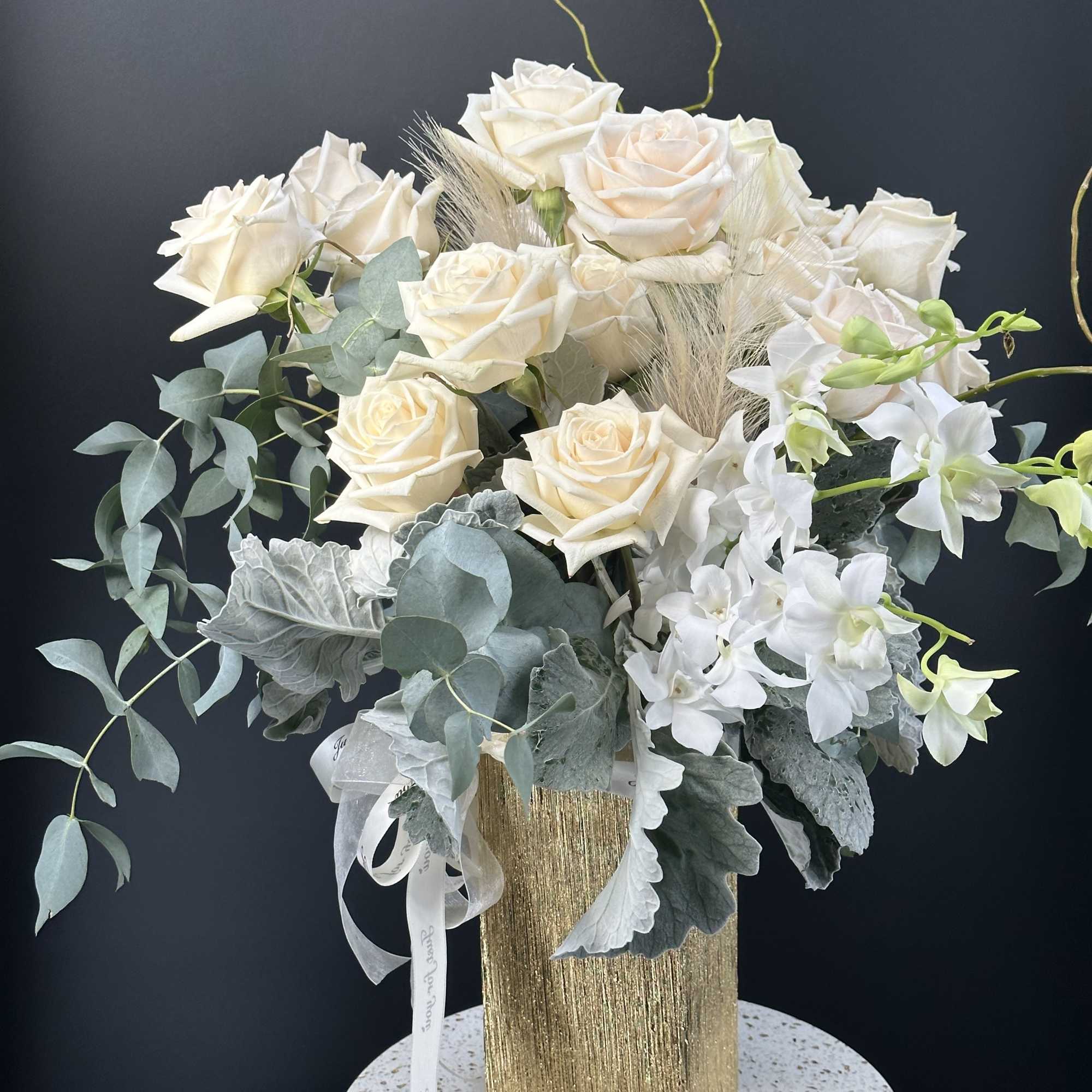 Cream roses and white orchids in a gold vase with silvery foliage, photo 9 of 11