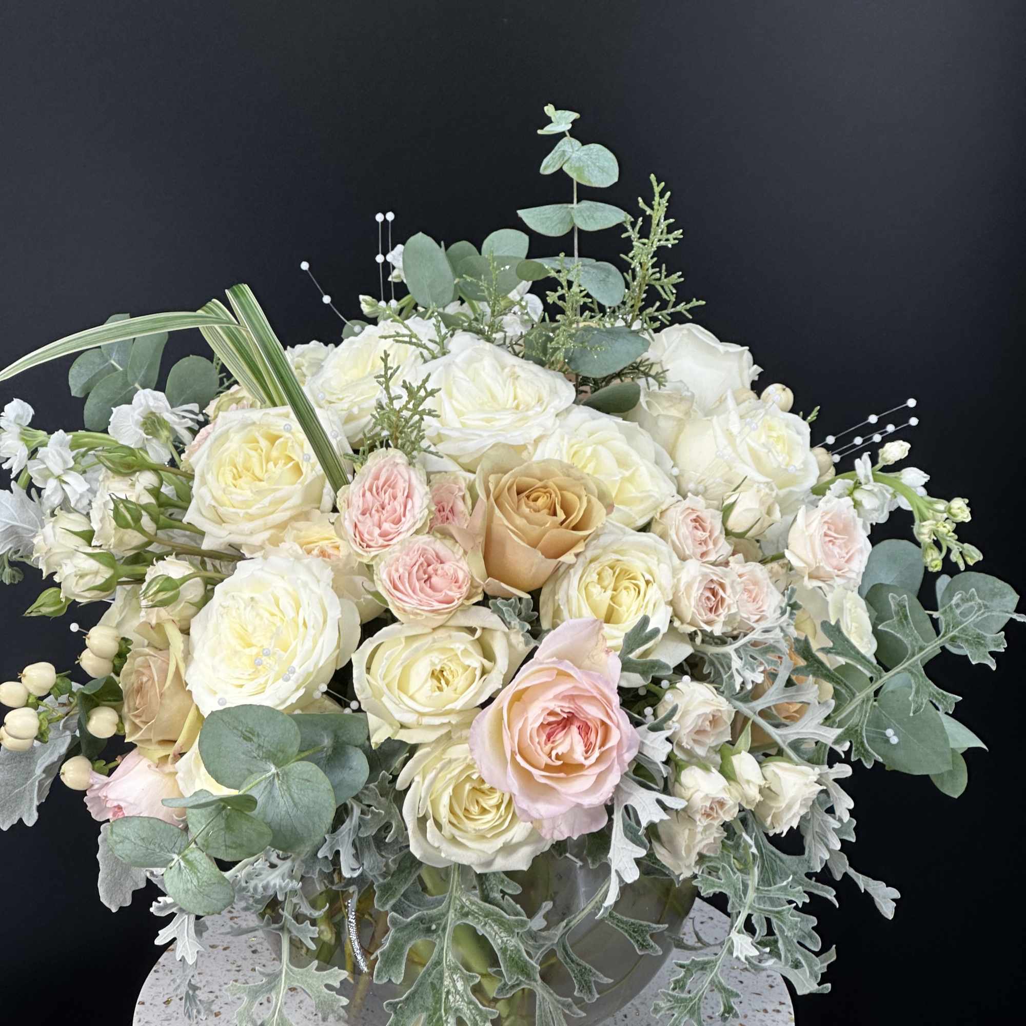 Cream and blush rose arrangement in a glass vase with eucalyptus
