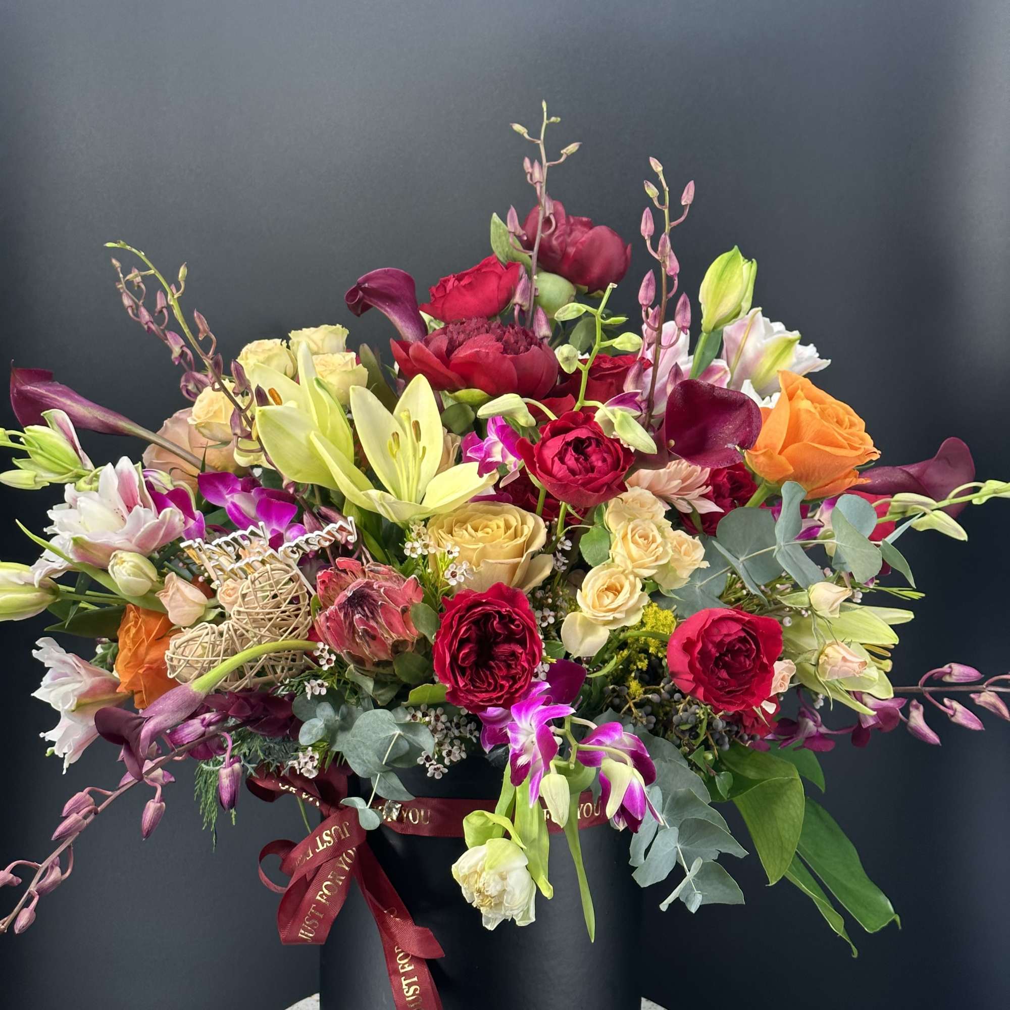 Mixed bouquet in a black hat box with roses, lilies, and orchids
