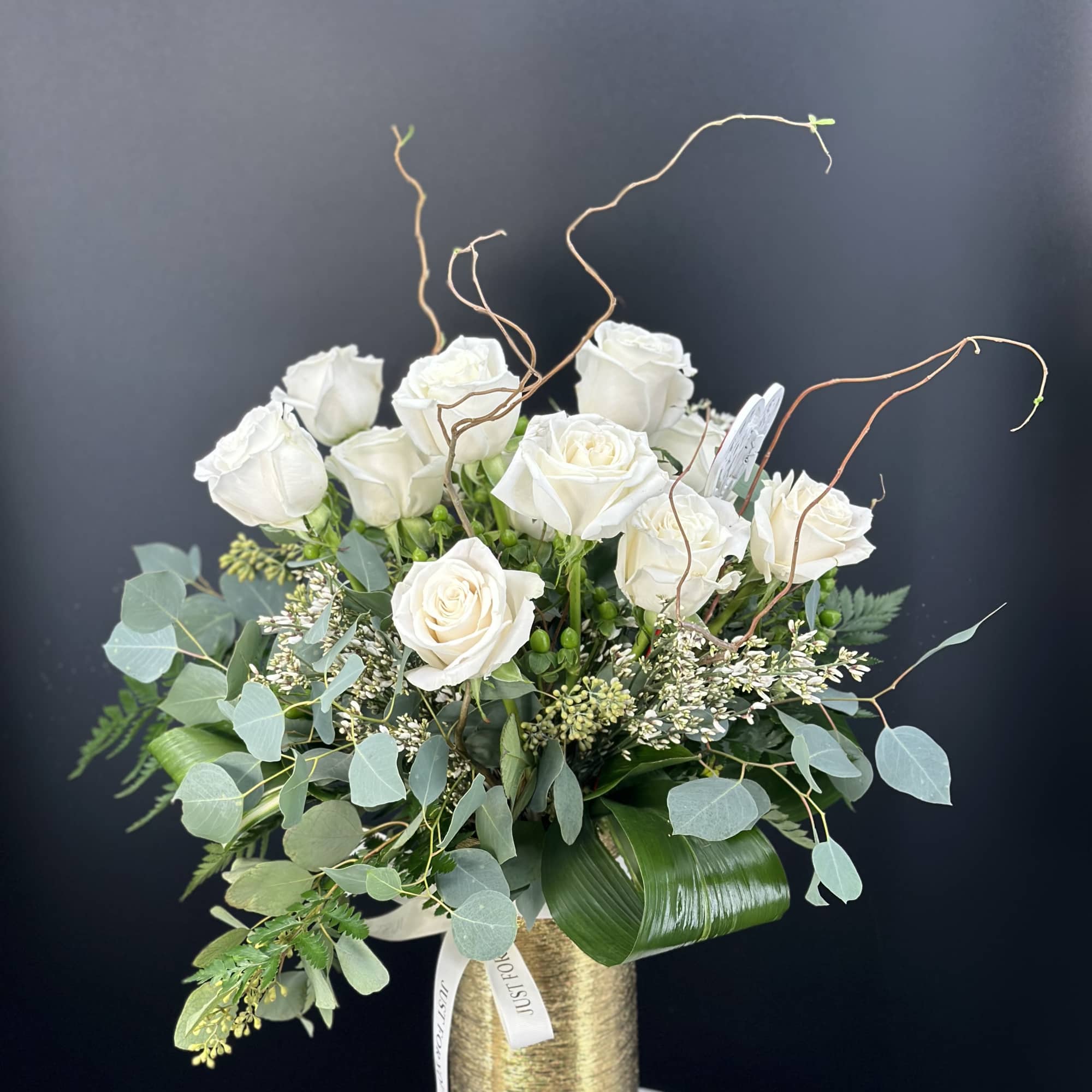White rose arrangement in a gold vase with eucalyptus and curly branches
