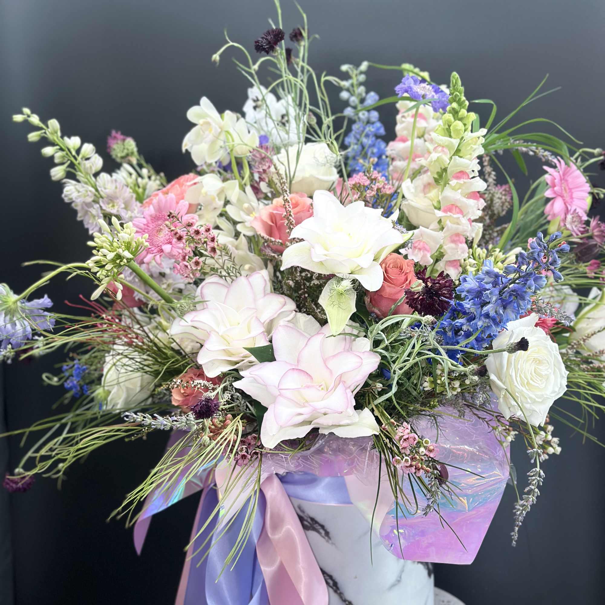Large pastel bouquet in a marble-patterned hatbox with pink and lavender ribbons