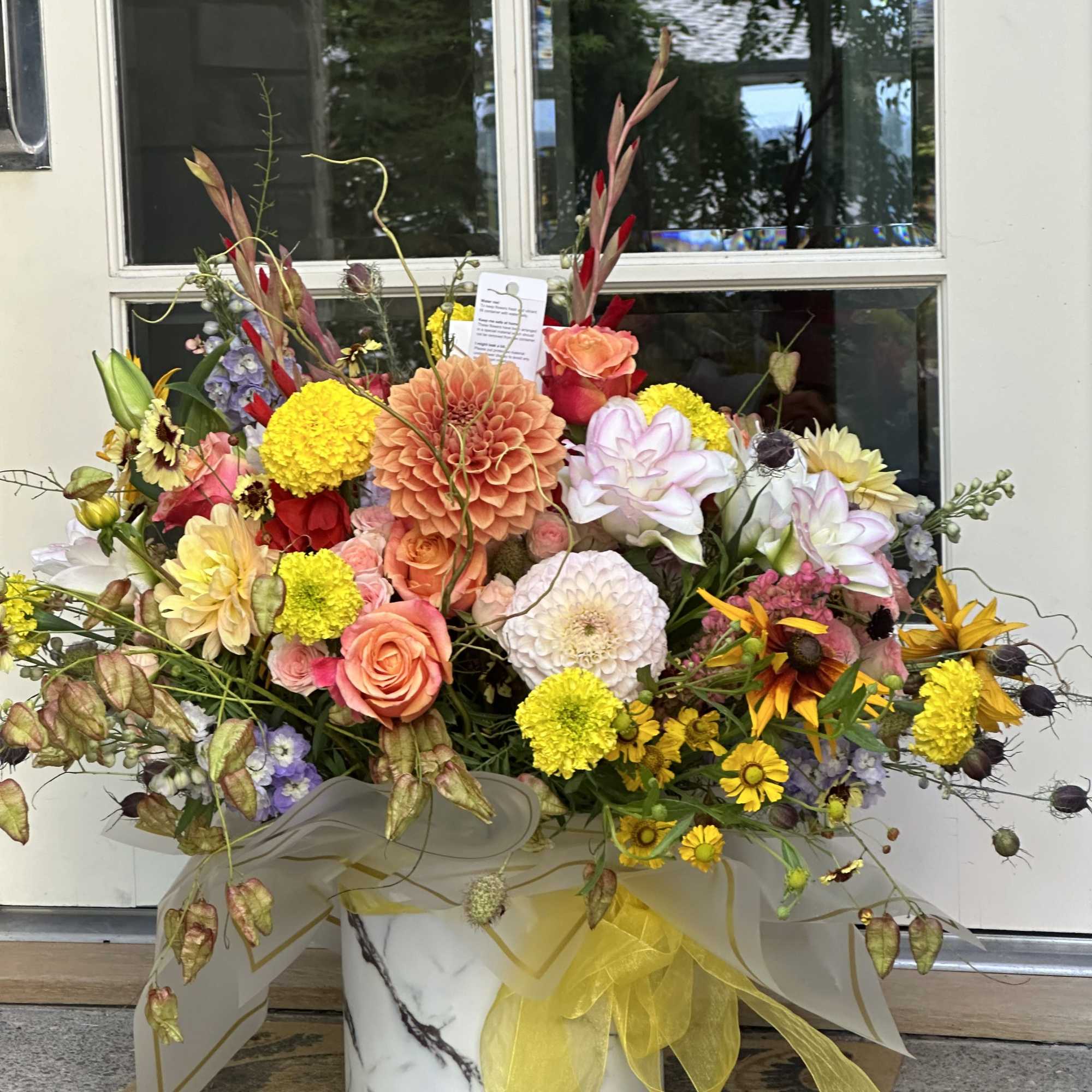 Large mixed flower arrangement in a marble-print box with yellow ribbon