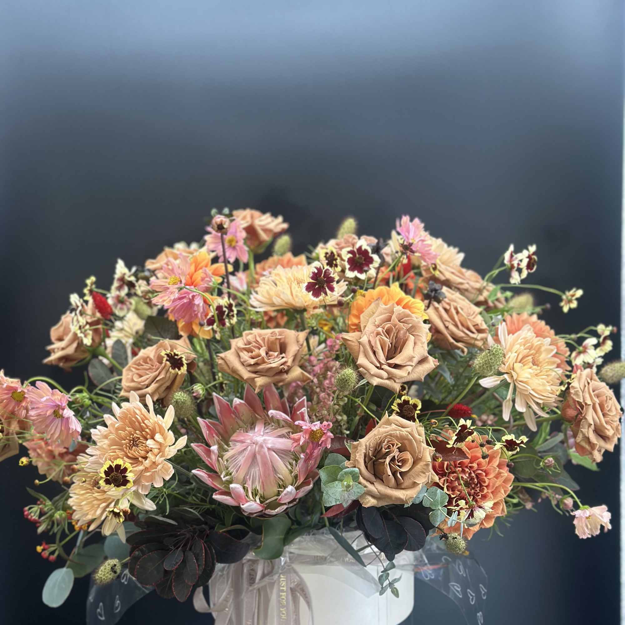 Large mixed bouquet in a clear vase with peach, pink, and cream flowers