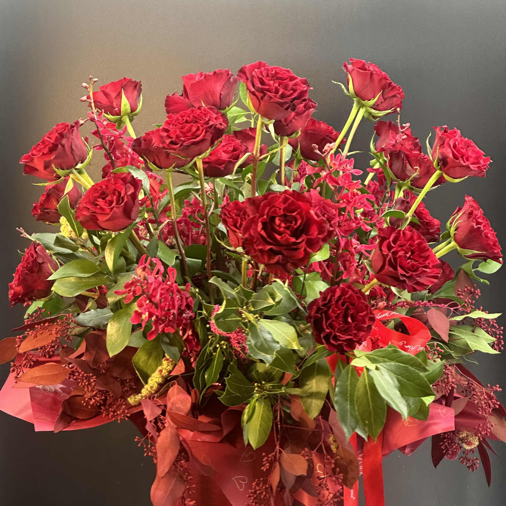 Red roses arranged in a tall red hatbox with ribbon accents