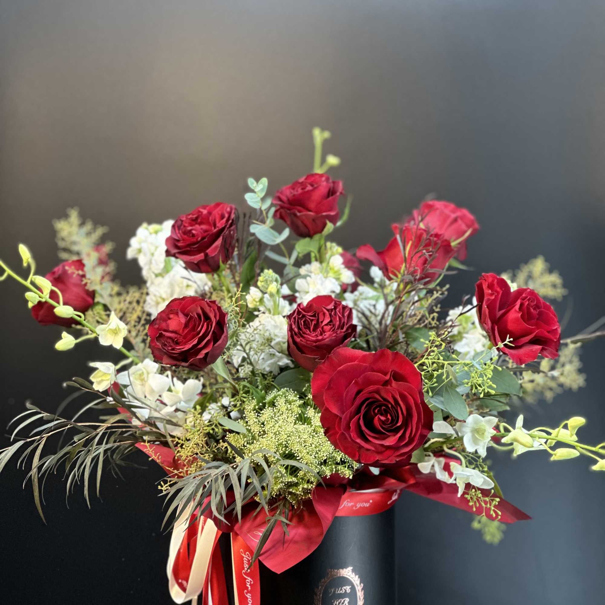 Red roses arranged in a black hatbox with white accent flowers and ribbon