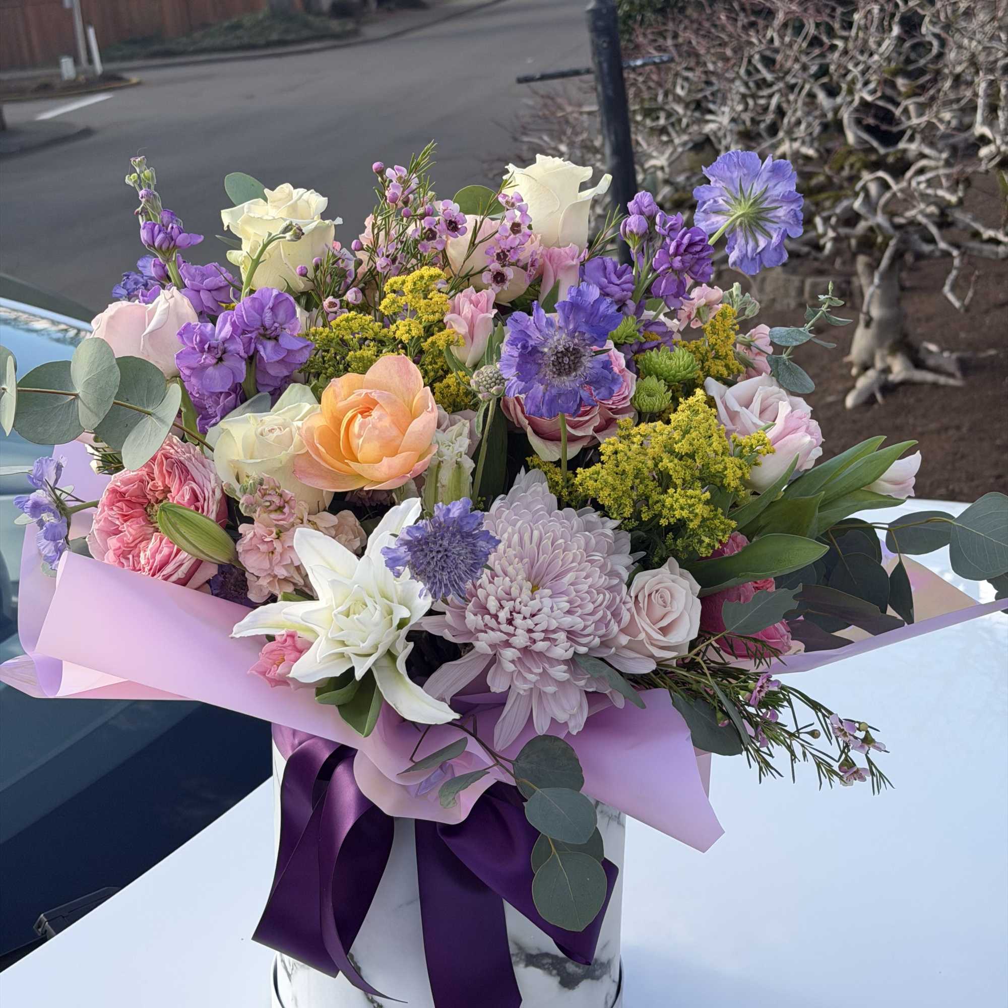 Mixed bouquet of pastel flowers in a marble-patterned box with a purple ribbon