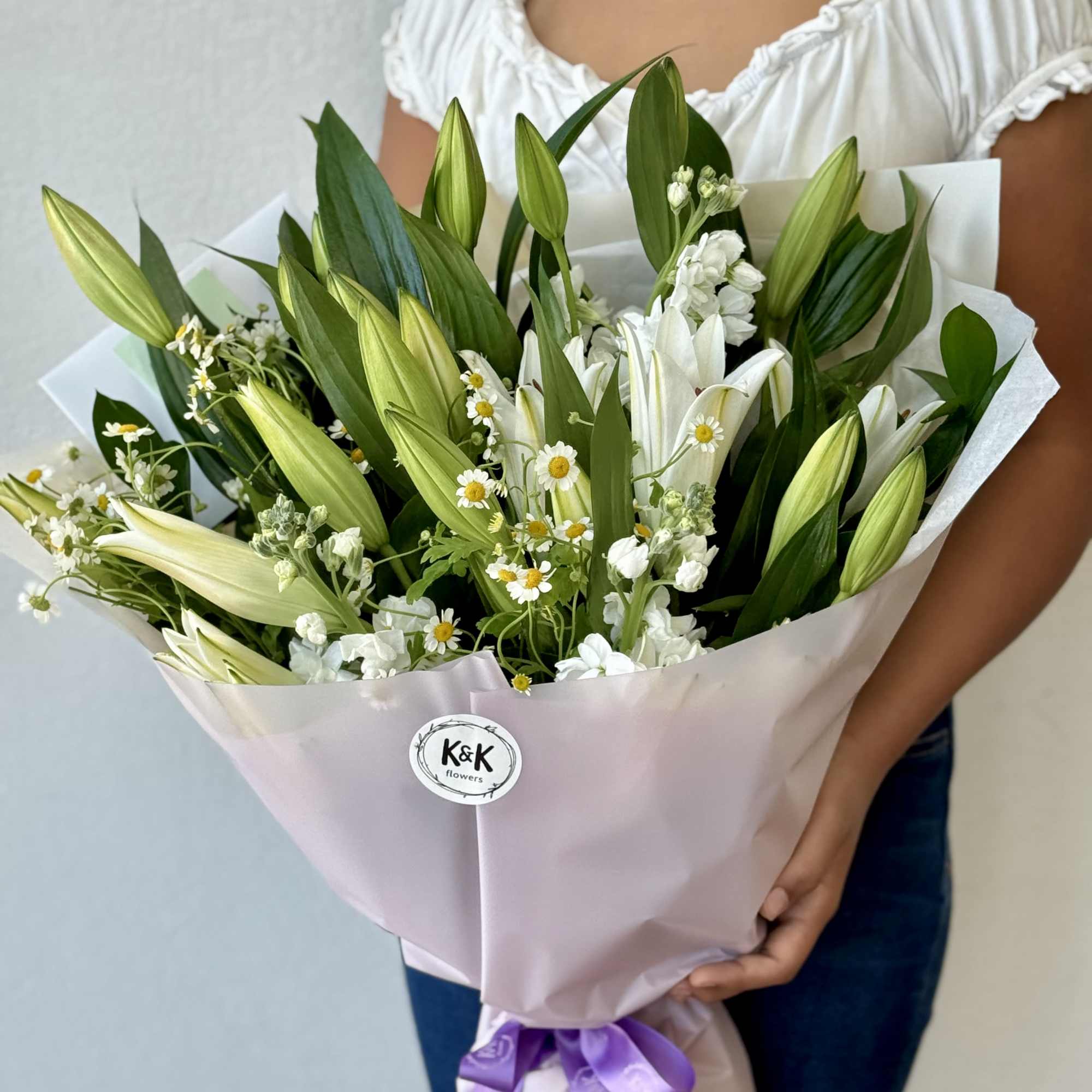 Bouquet of white lilies and small white daisies wrapped in pink paper