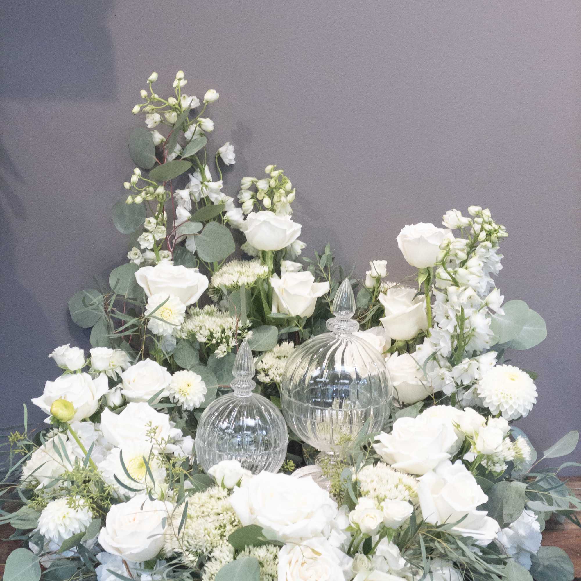 Low white flower arrangement with roses and mums surrounding two clear glass lidded jars.