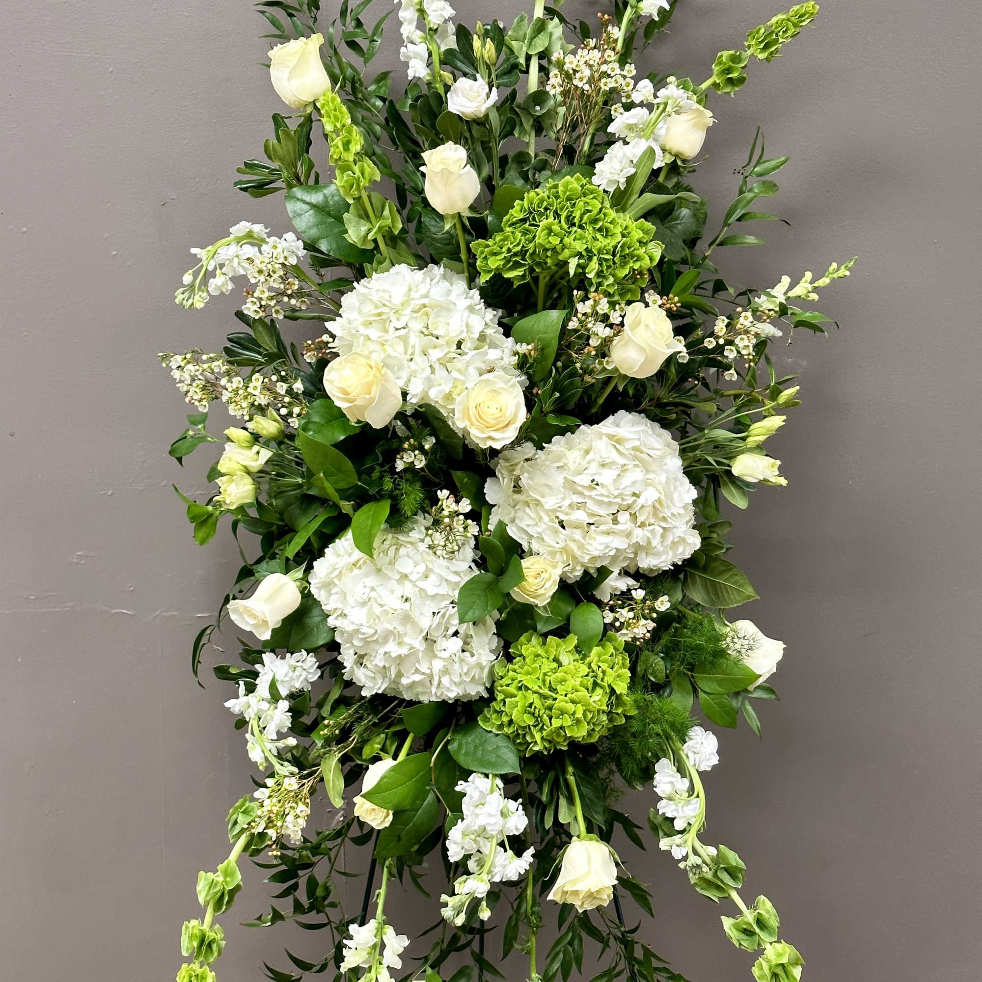 Tall standing spray of white roses and hydrangeas with green accents on an easel stand