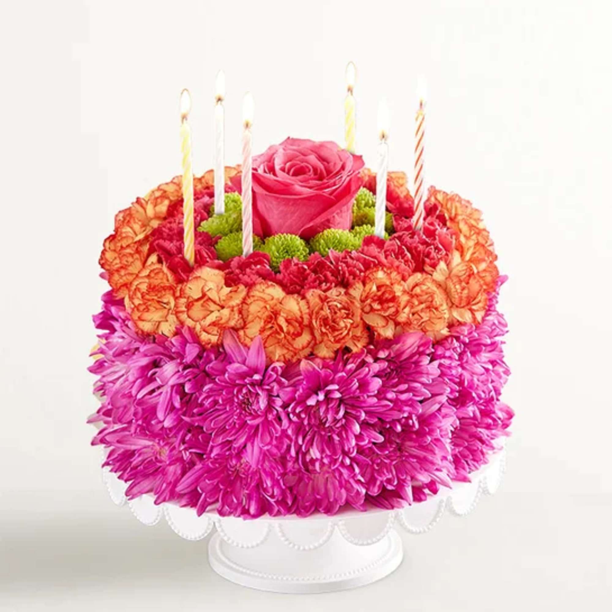 Round flower cake with a pink rose center and striped candles on a white stand
