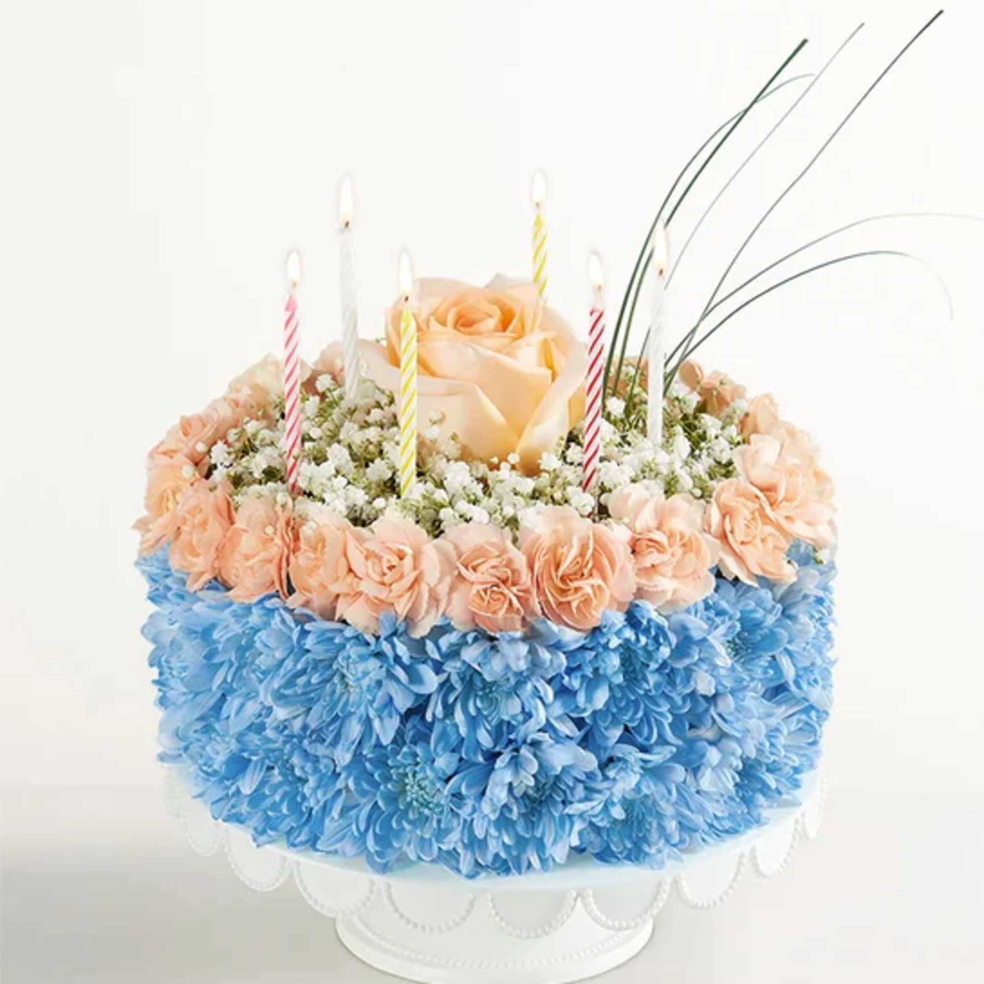 Round floral cake with peach roses, blue flowers, and striped candles