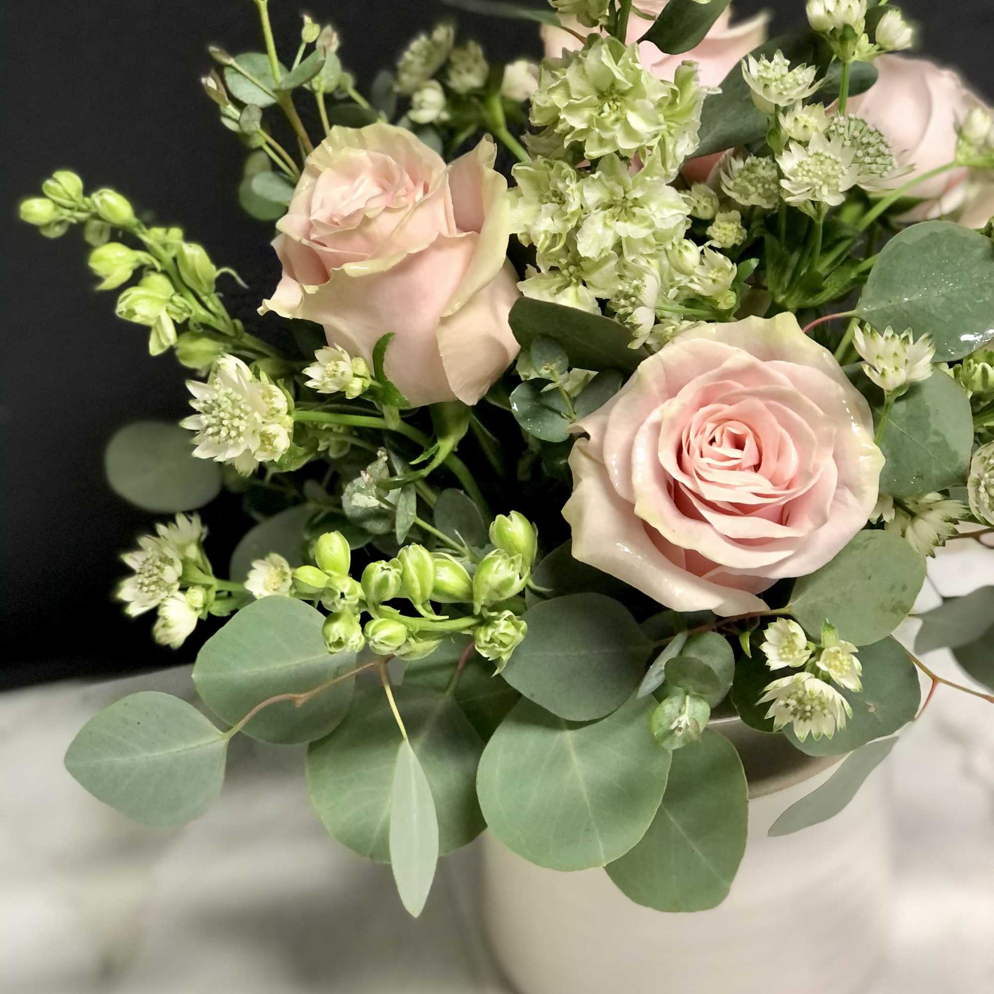 Blush roses and pale green flowers arranged in a white vase