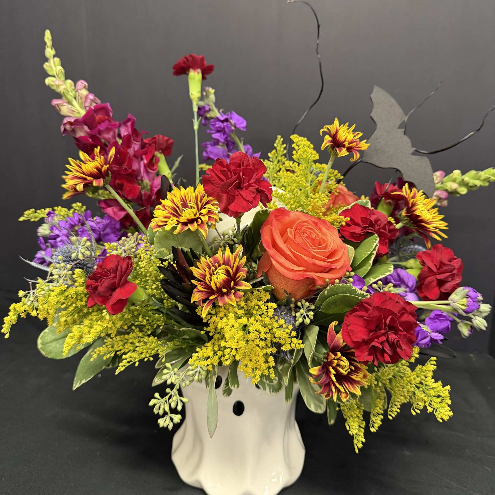 Colorful floral arrangement in a white ceramic vase with roses, carnations, and mixed blooms