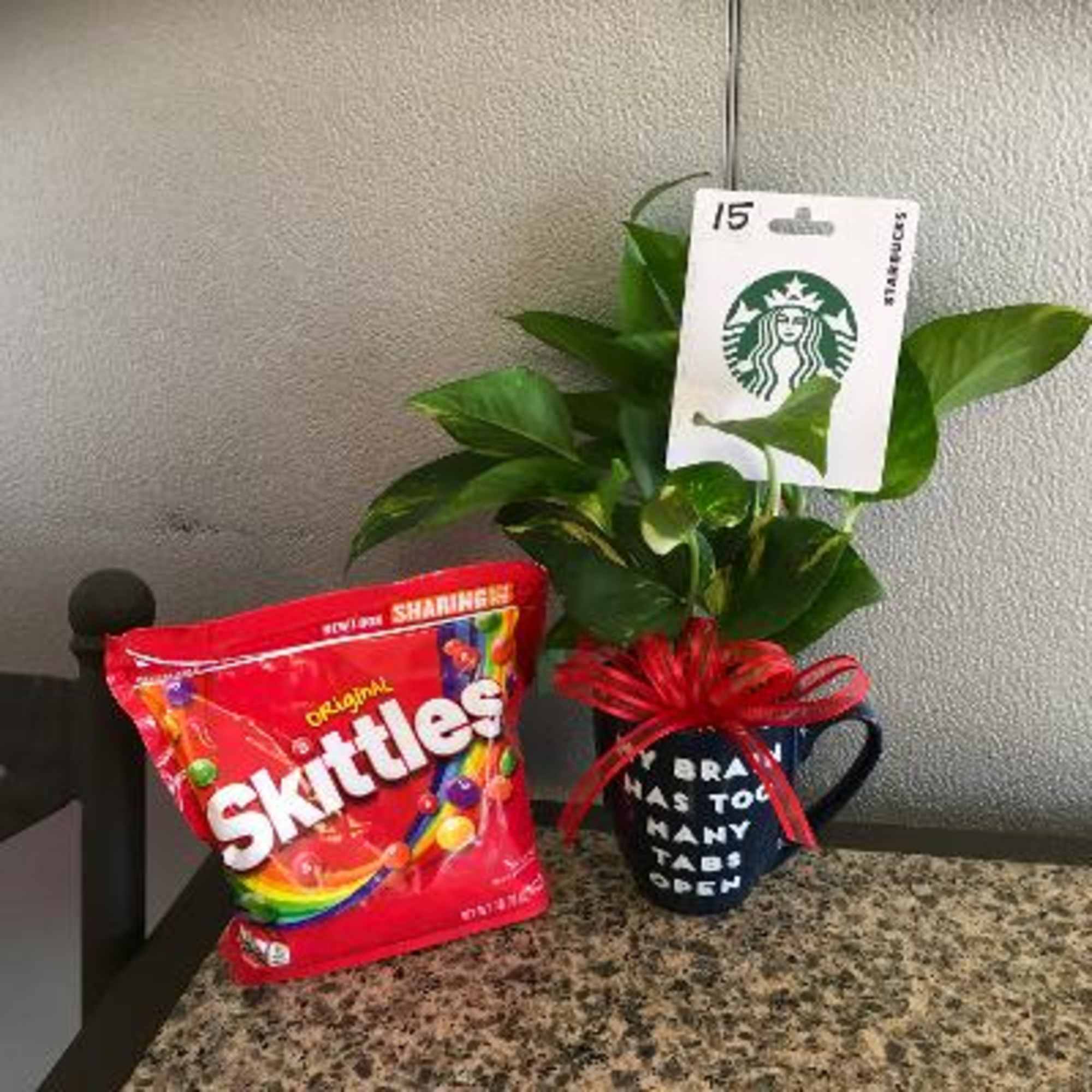 Potted green plant in a Starbucks mug beside a bag of Skittles candy