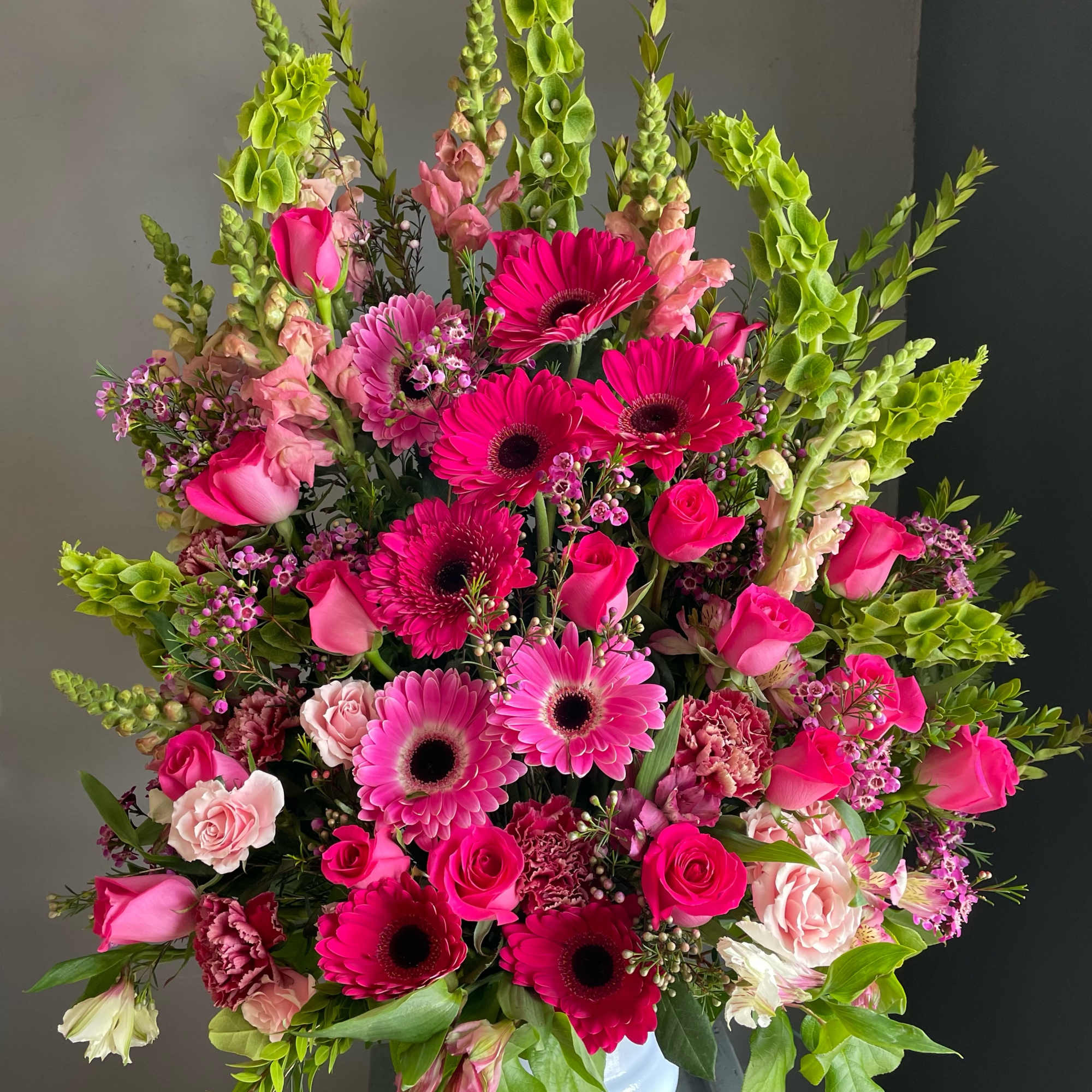Large pink and green floral arrangement in a white vase