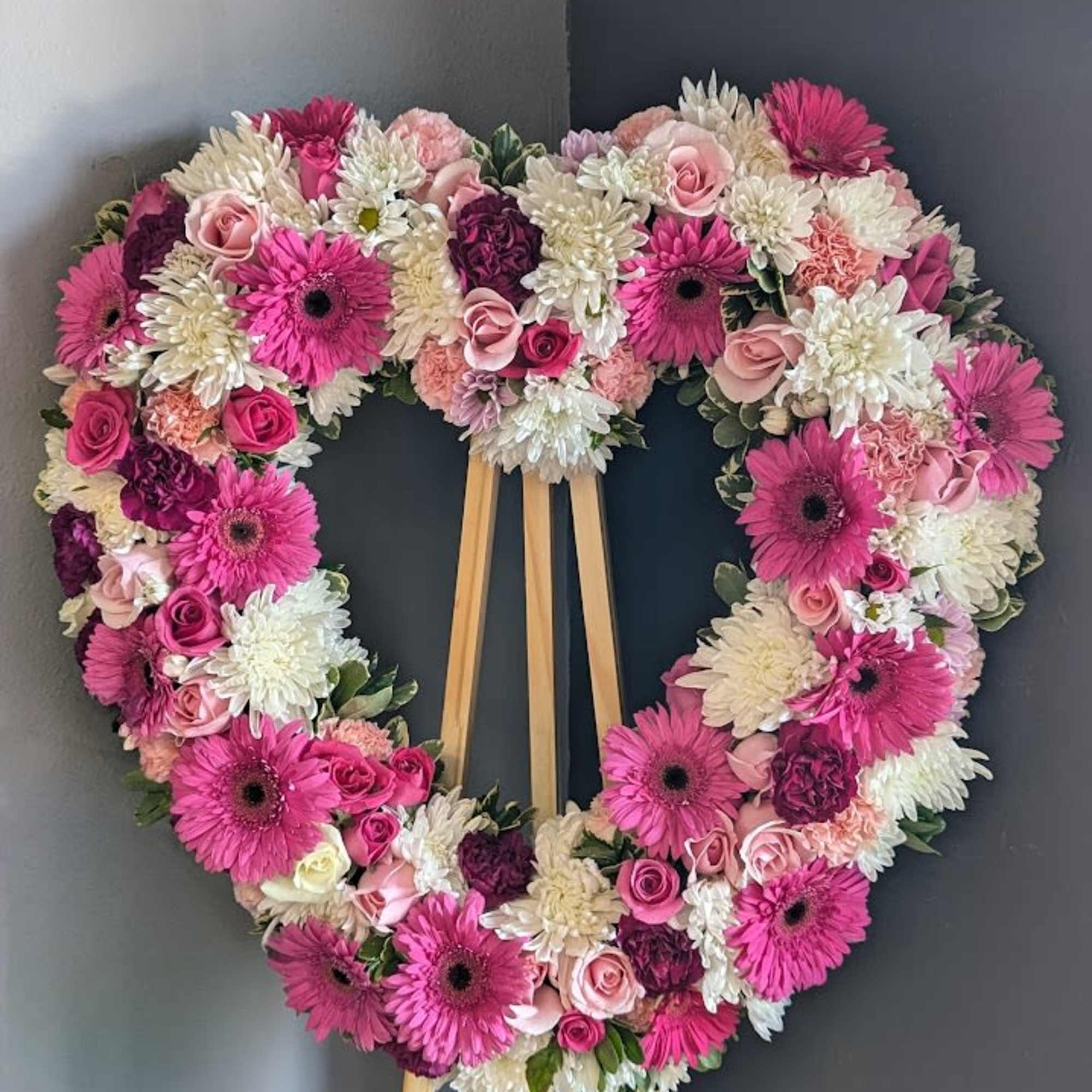 Heart-shaped floral wreath on a wooden easel with pink and white blooms