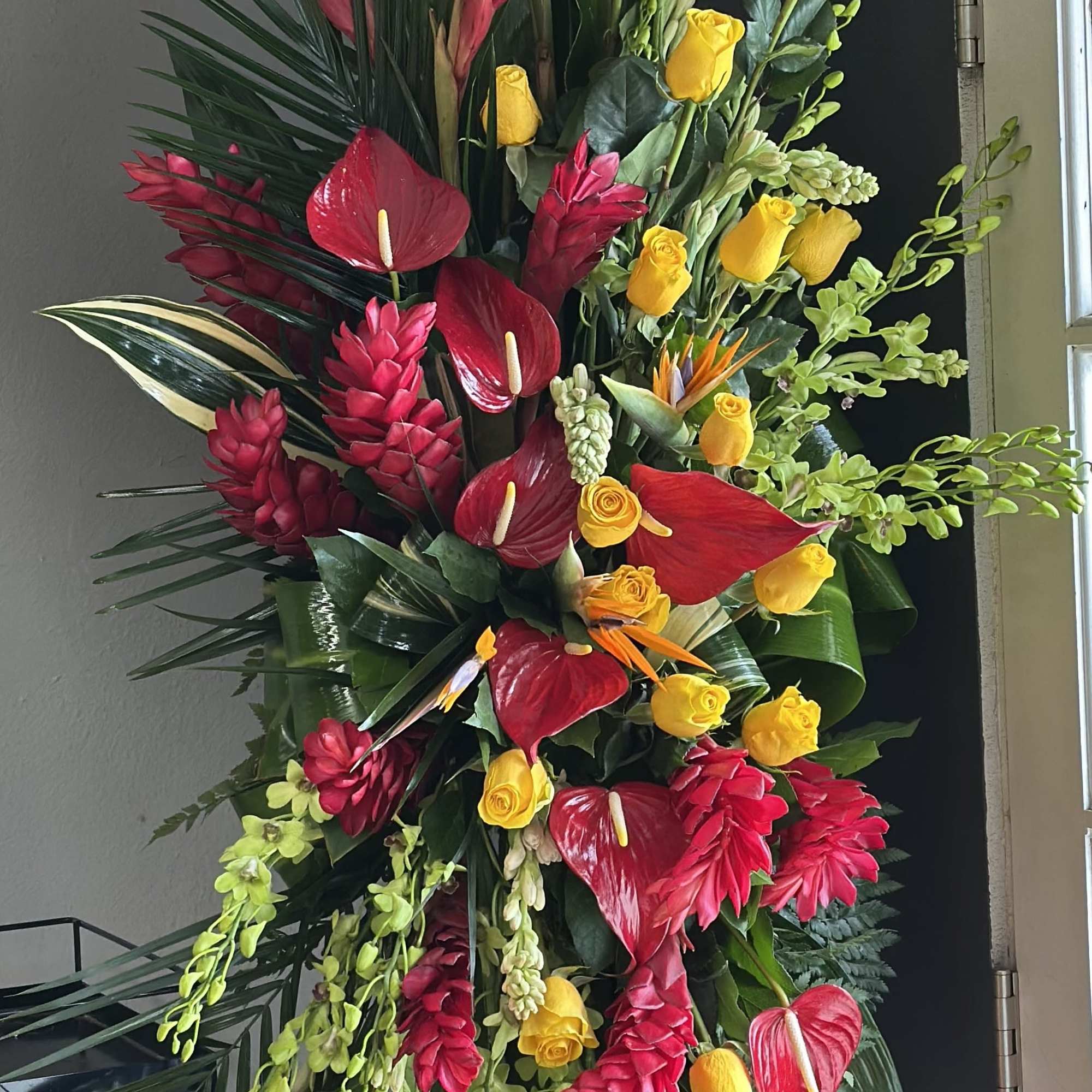 Tall tropical standing arrangement with red anthuriums and yellow roses
