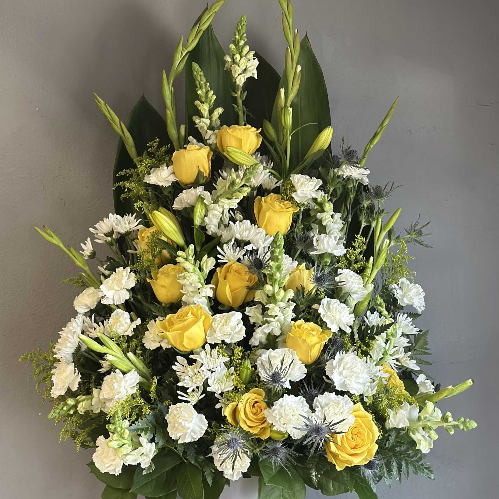 Yellow roses and white flowers arranged in a white pedestal vase
