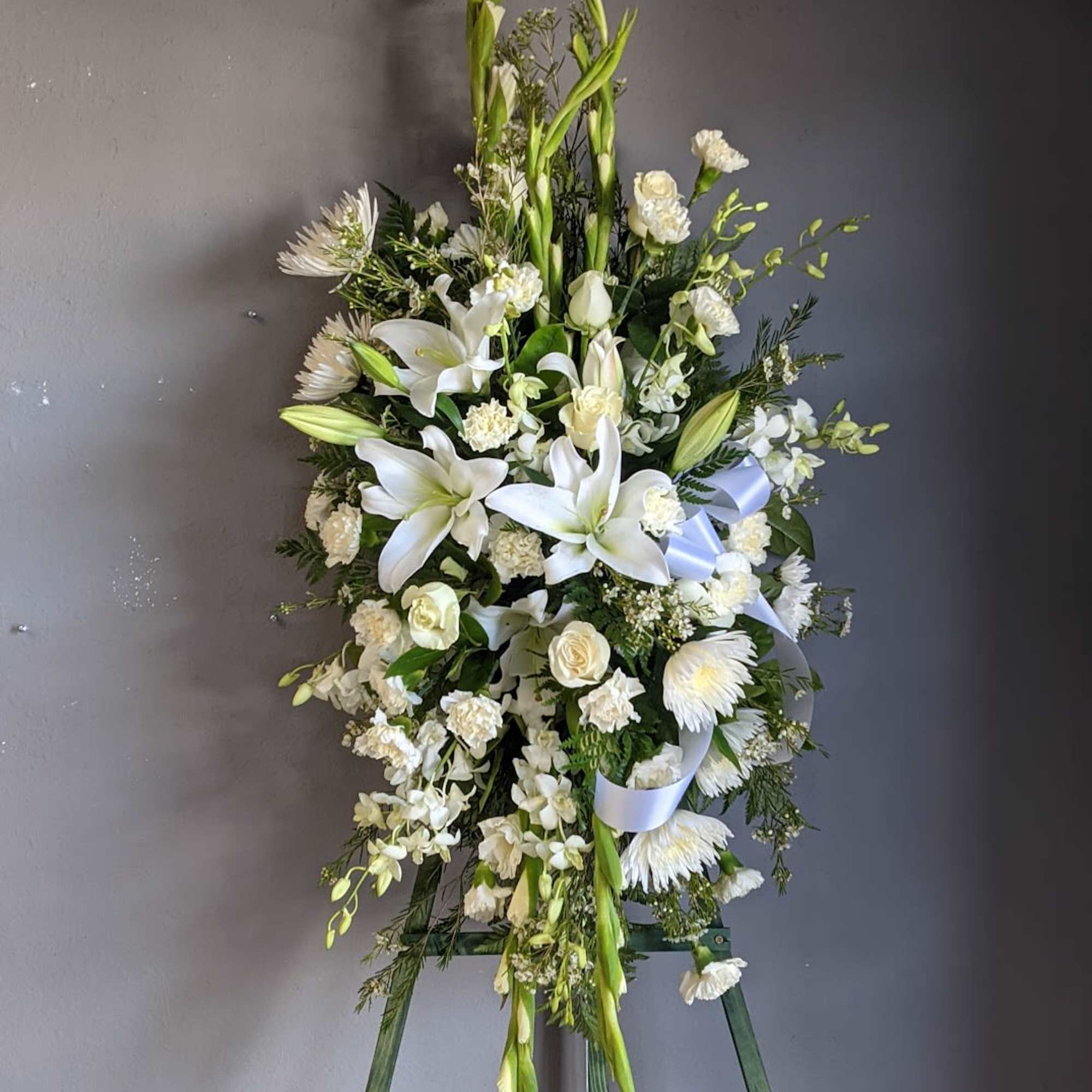 White floral standing spray on an easel with lilies and roses
