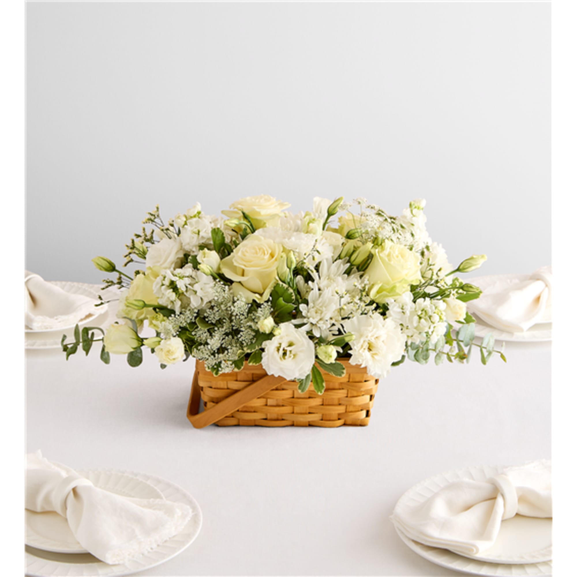 Creamy white floral arrangement in a woven basket on a table