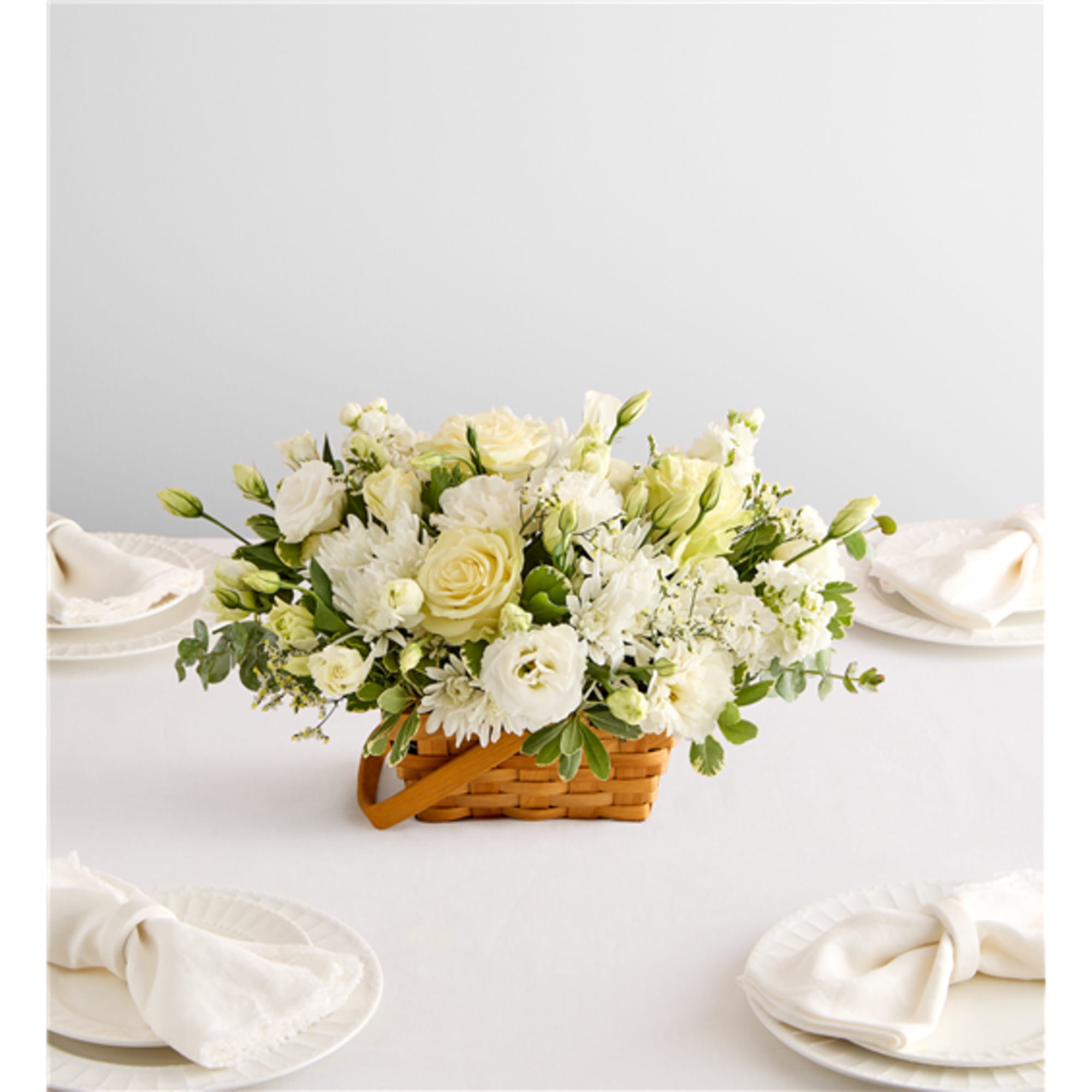 Cream and white flower arrangement in a woven basket on a table
