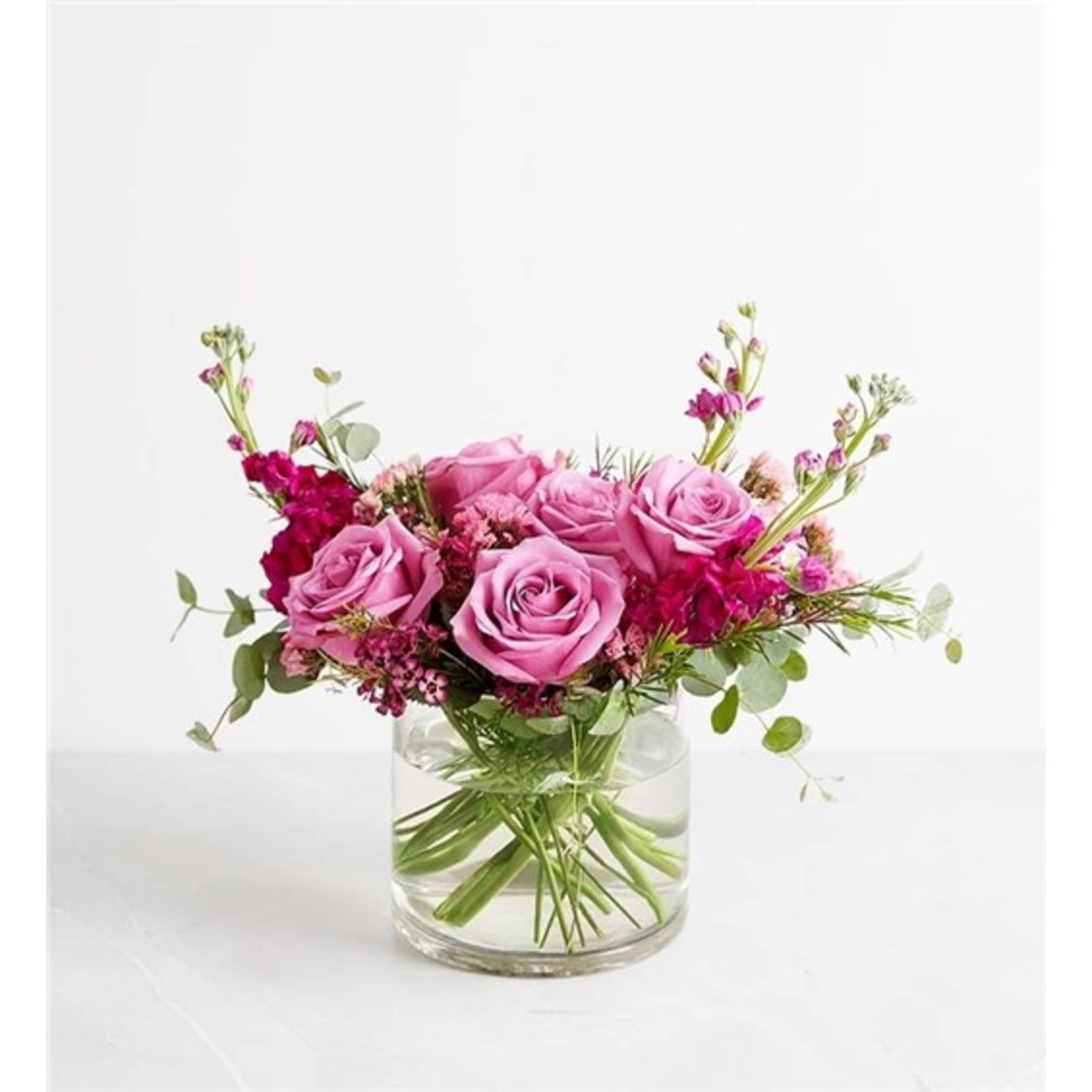 Pink roses and magenta flowers arranged in a clear glass vase