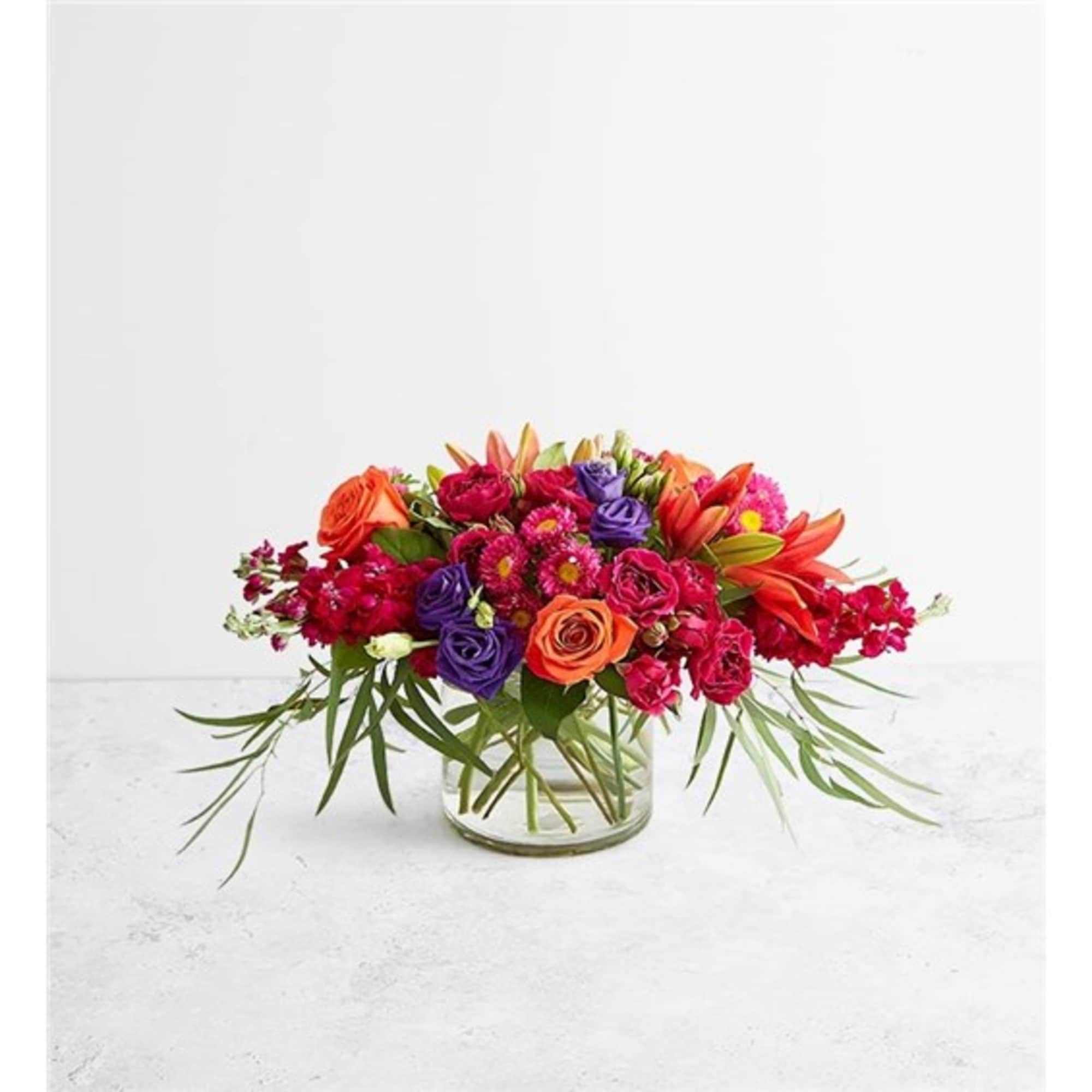 Bright mixed bouquet in a clear glass vase with orange, pink, and purple flowers
