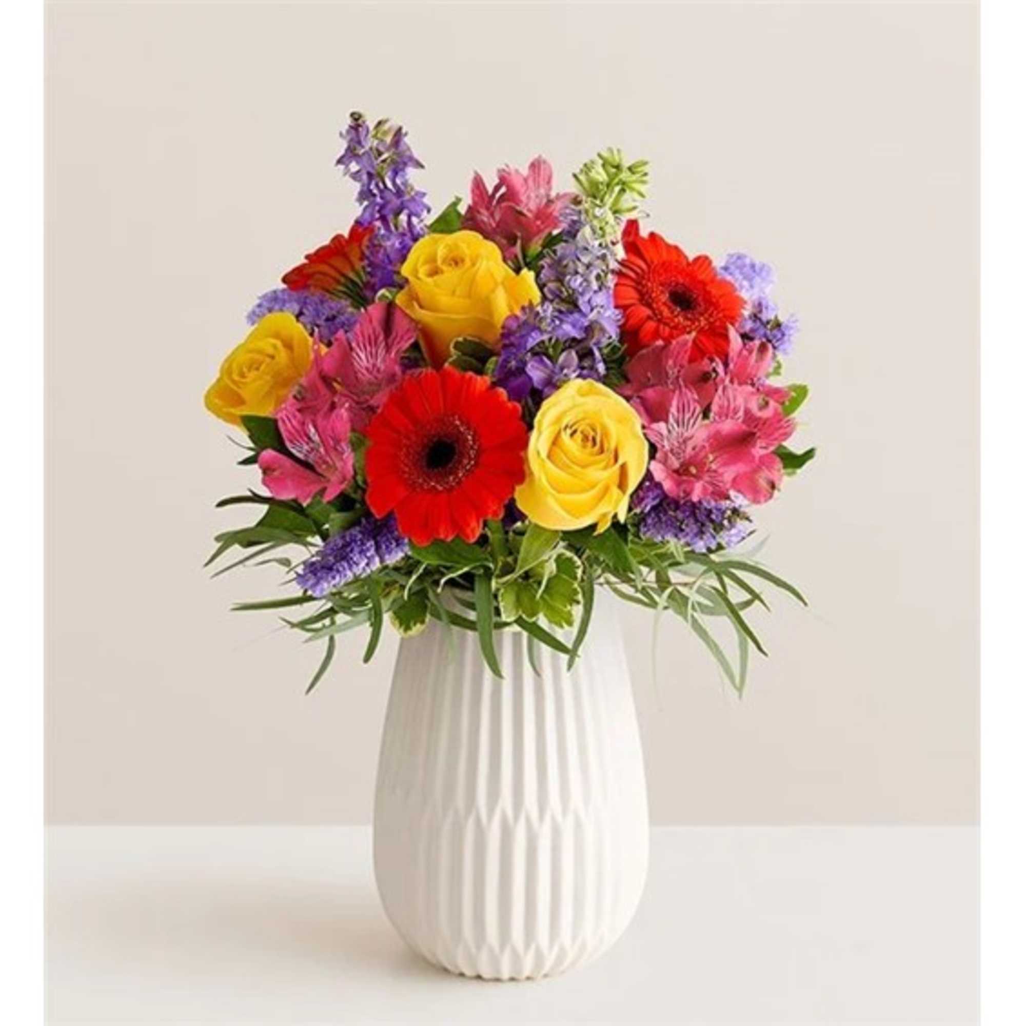 Colorful bouquet of roses, gerbera daisies, and purple flowers in a white vase