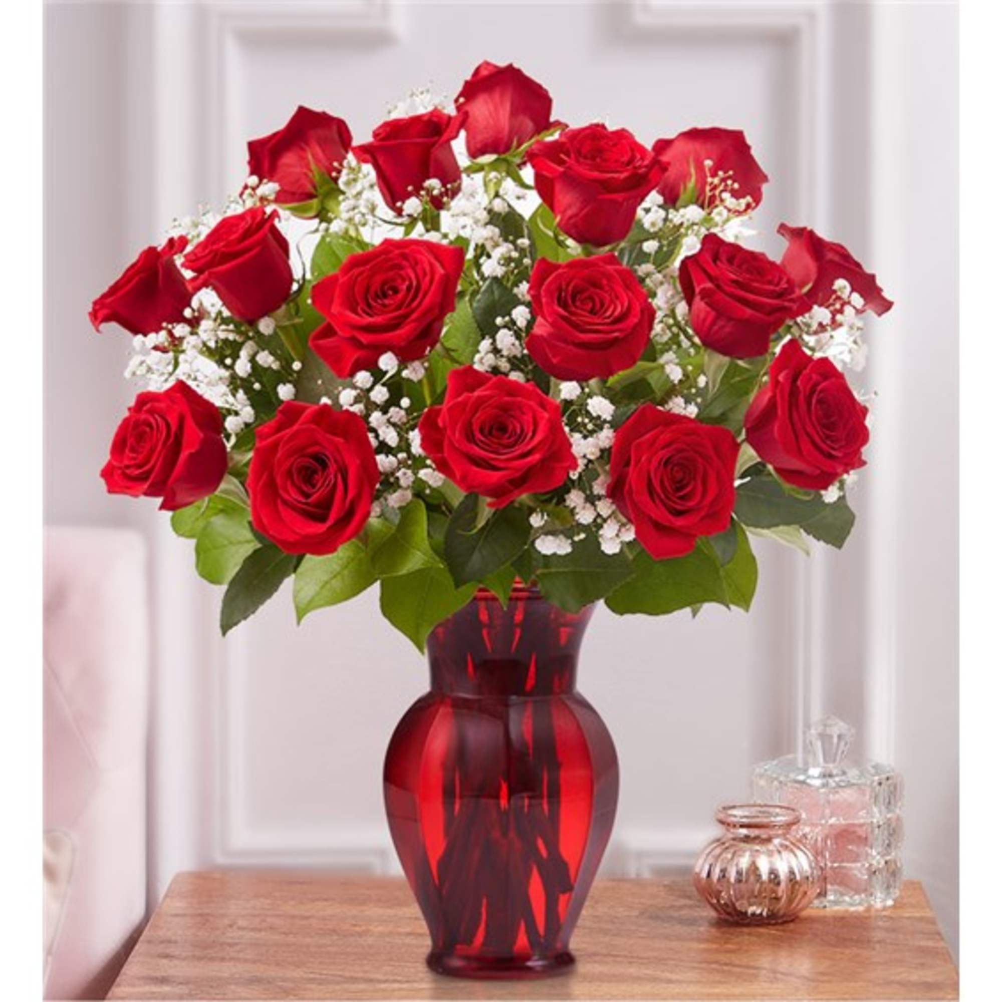 Red roses arranged in a red glass vase with white baby's breath