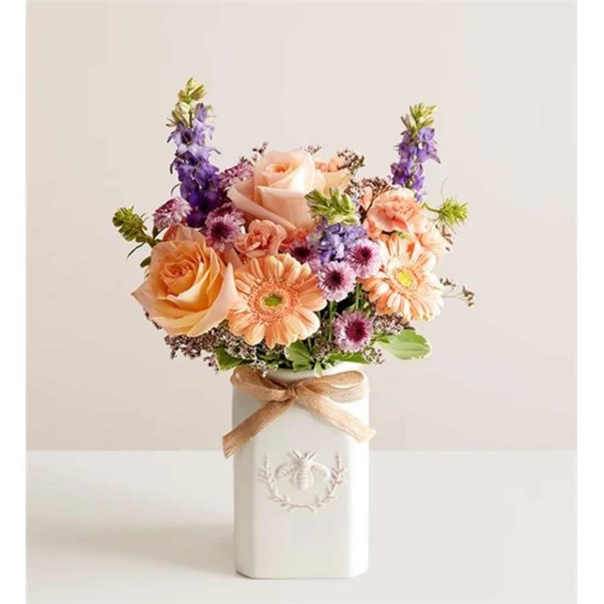 Peach roses and purple flowers in a white vase with a ribbon