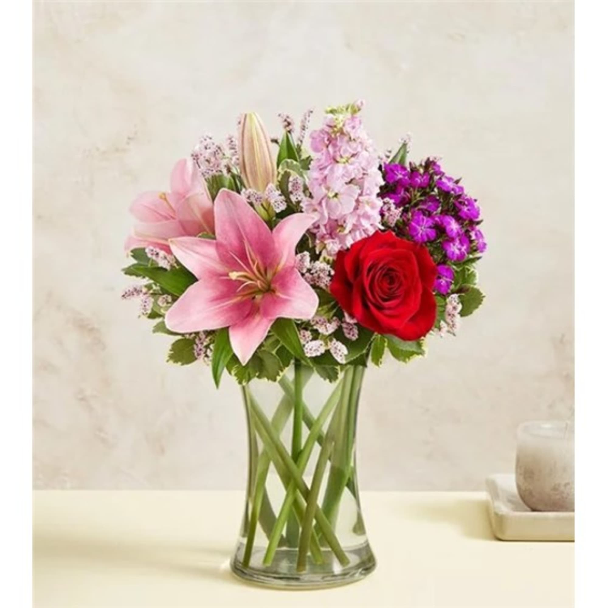 Pink lilies and a red rose in a clear glass vase