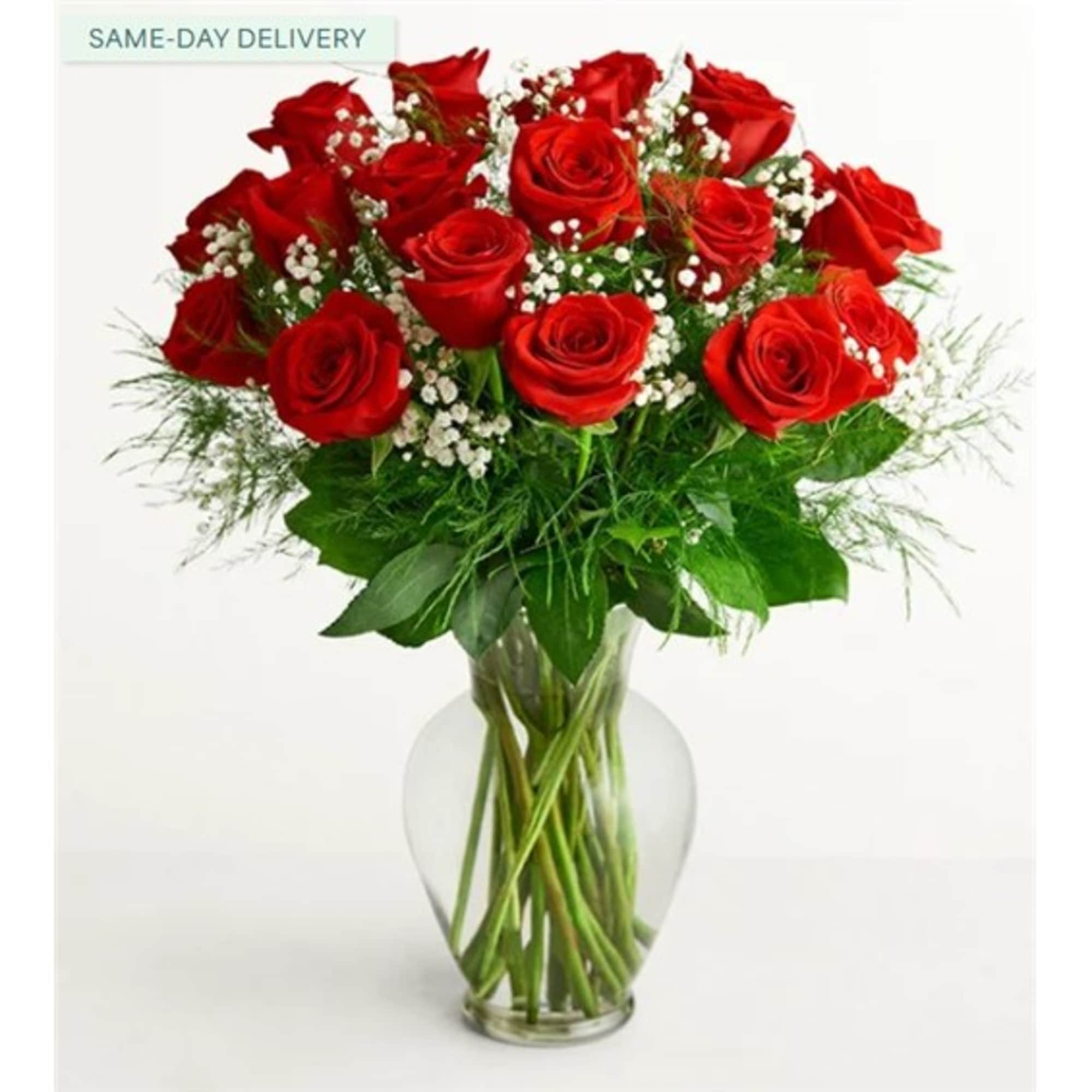 Red roses arranged in a clear glass vase with small white filler flowers
