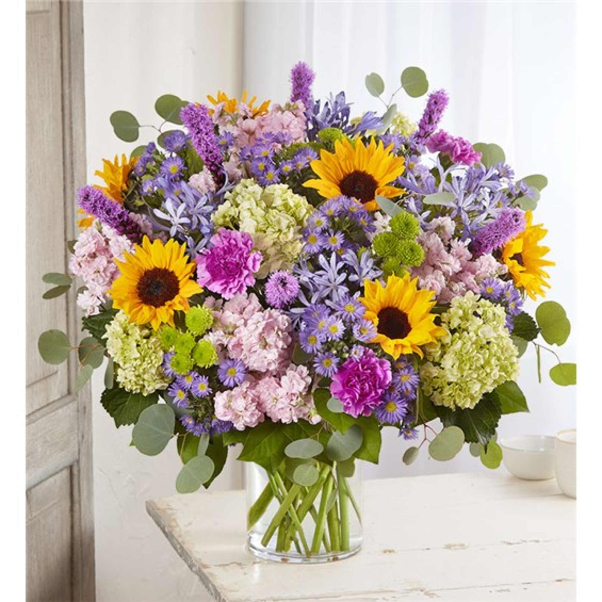 Mixed bouquet with sunflowers, purple flowers, and pink blooms in a glass vase