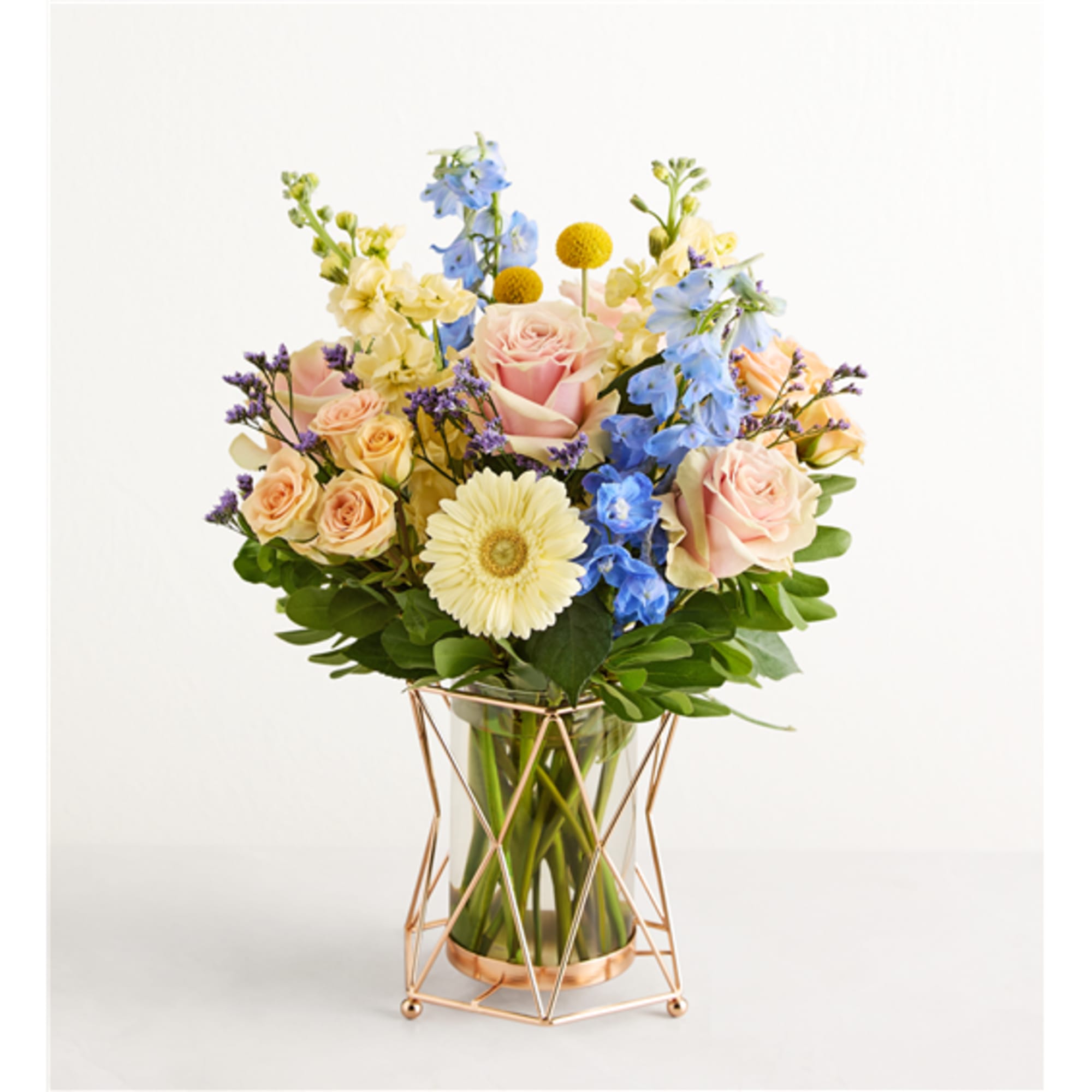 Pastel bouquet of roses, blue delphinium, and a white gerbera in a glass vase